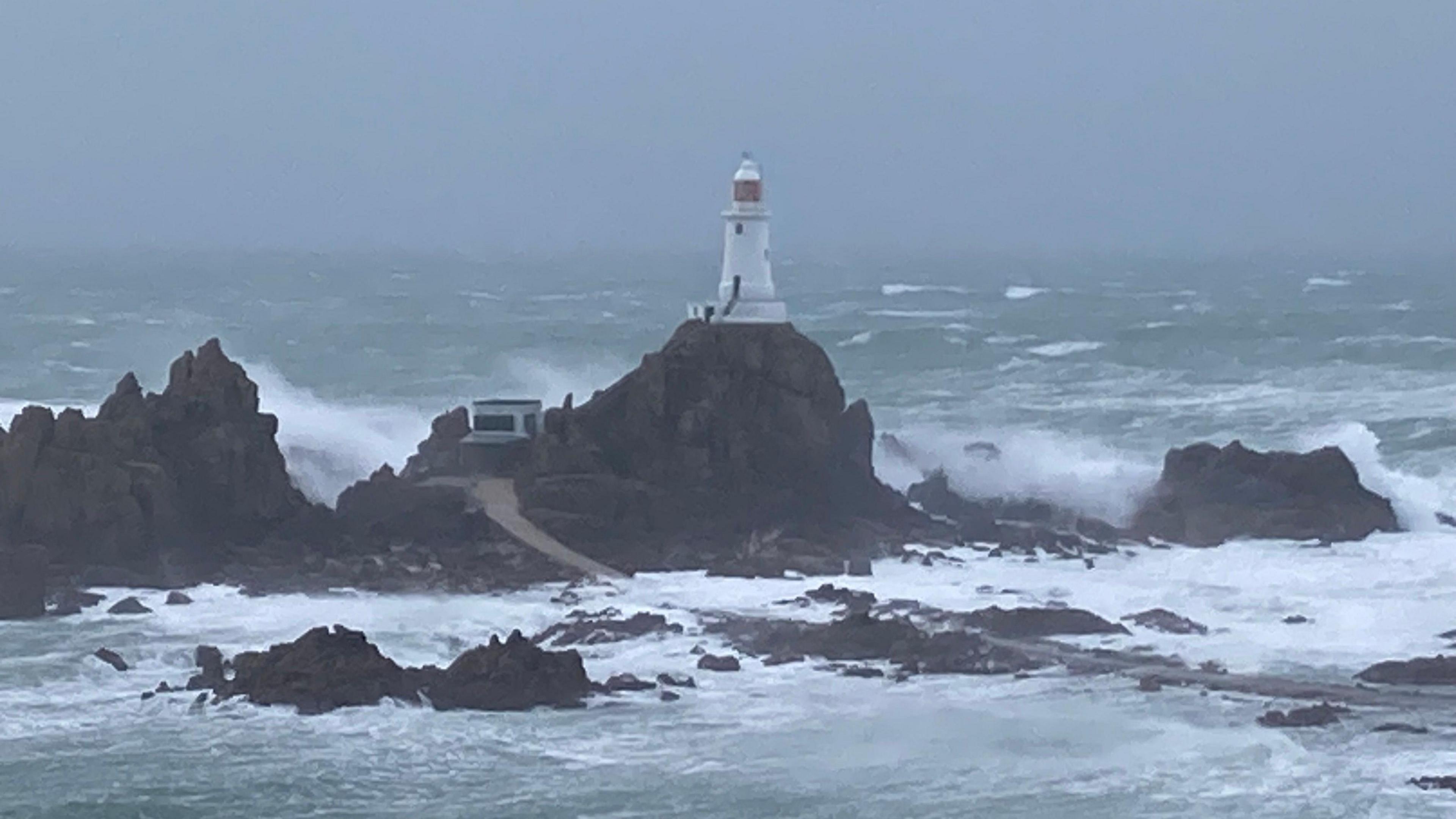 Waves splash over rocks beneath a lighthouse.