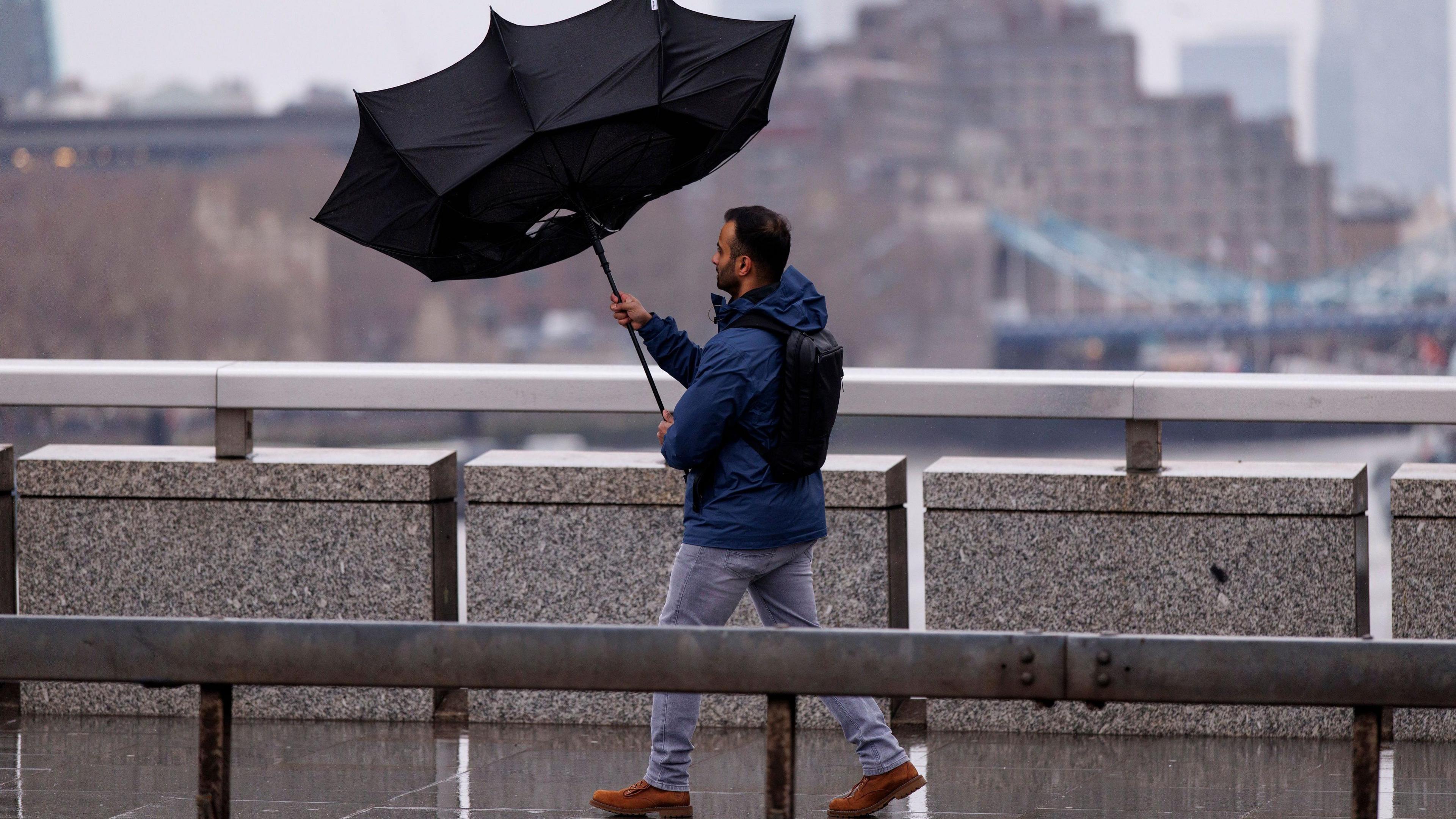 Man walks across bridge with inside out umbrella