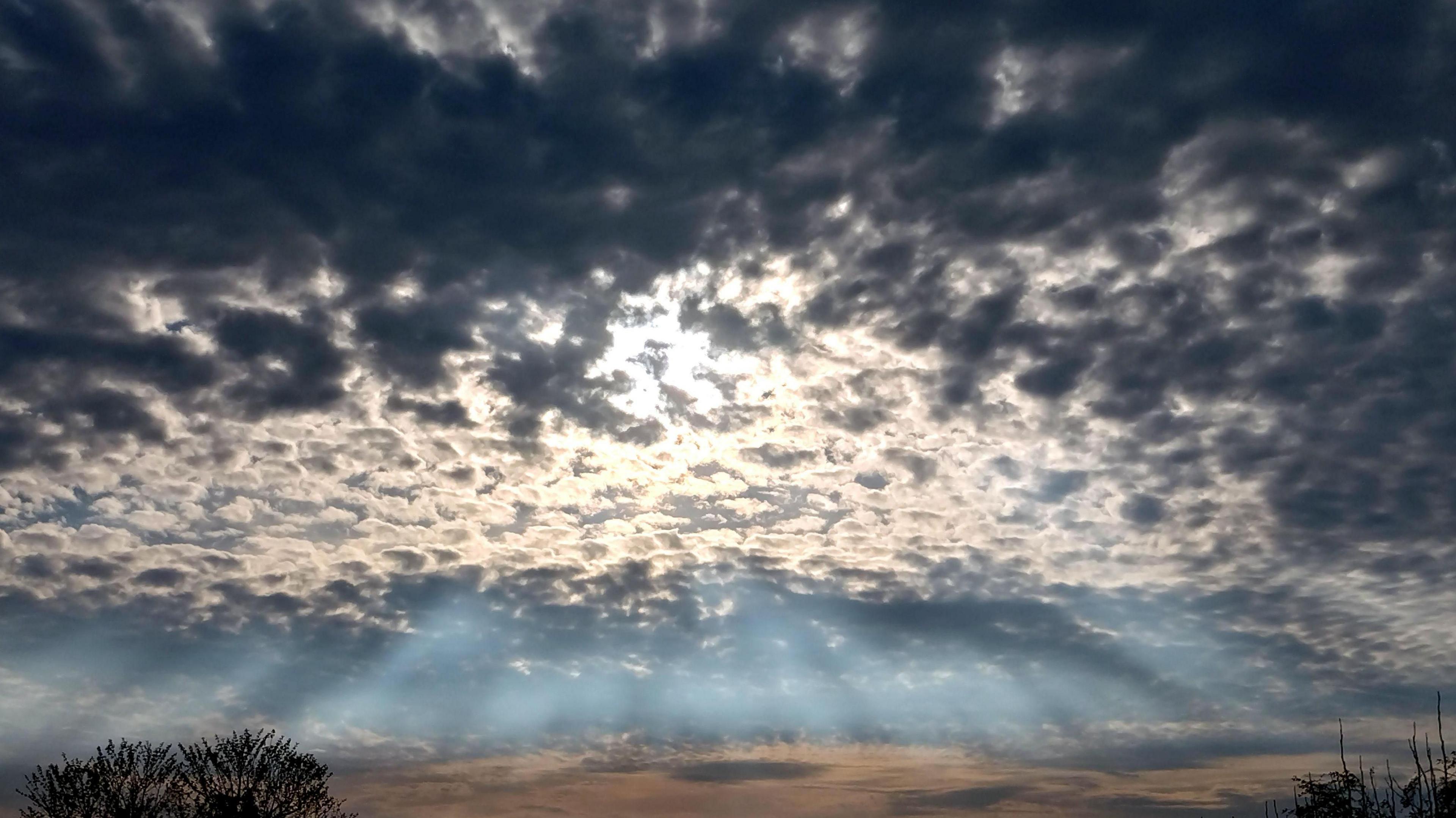 Dark and light grey cloud bubbling in the sky in front of the Sun reflecting crepuscular rays through the cloud