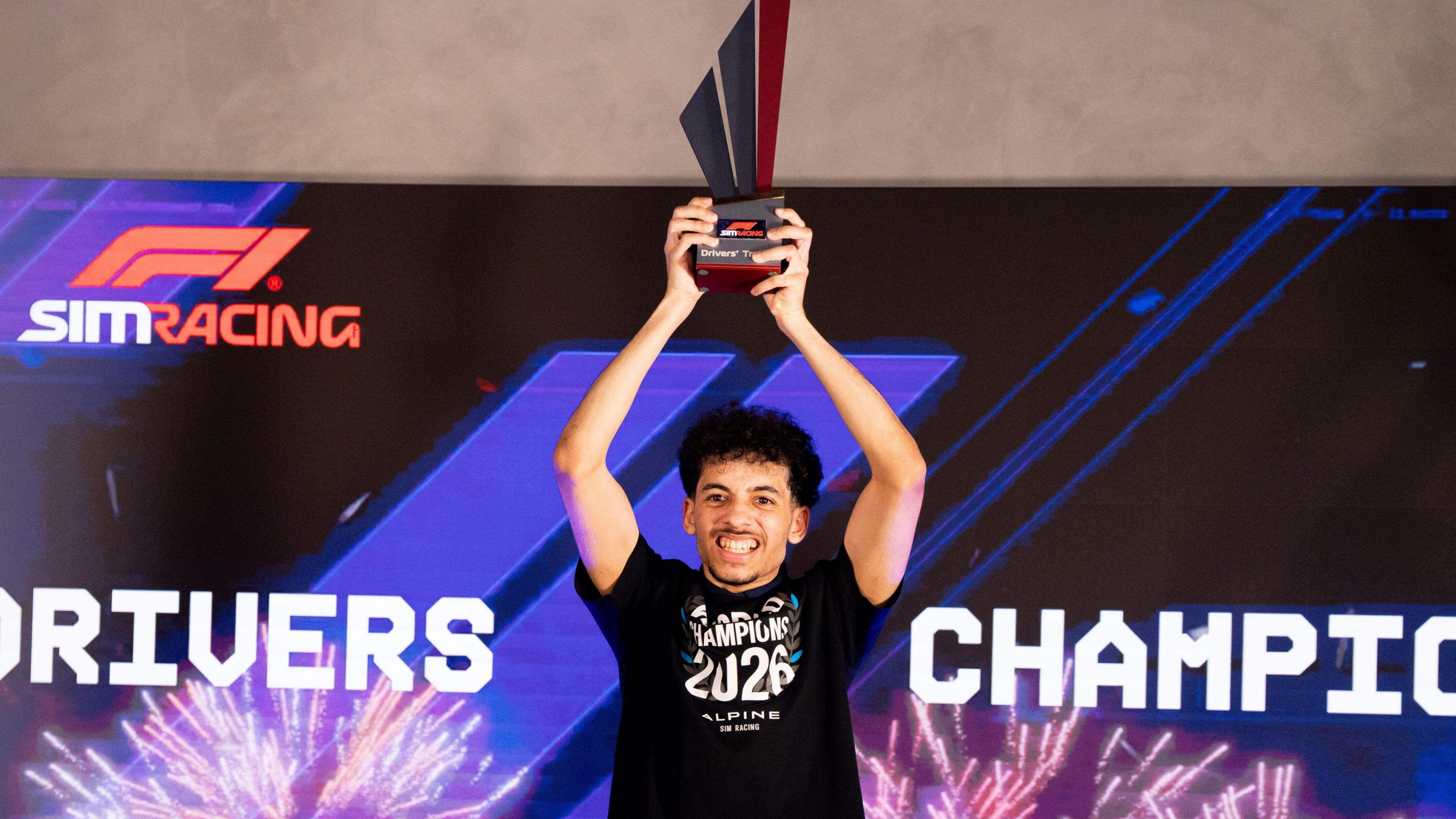 Otis Lawrence holding a trophy in the air. He is smiling. Otis has short dark hair and short stubble, and is wearing a black t shirt with the Words World Champion 2026 written on it.