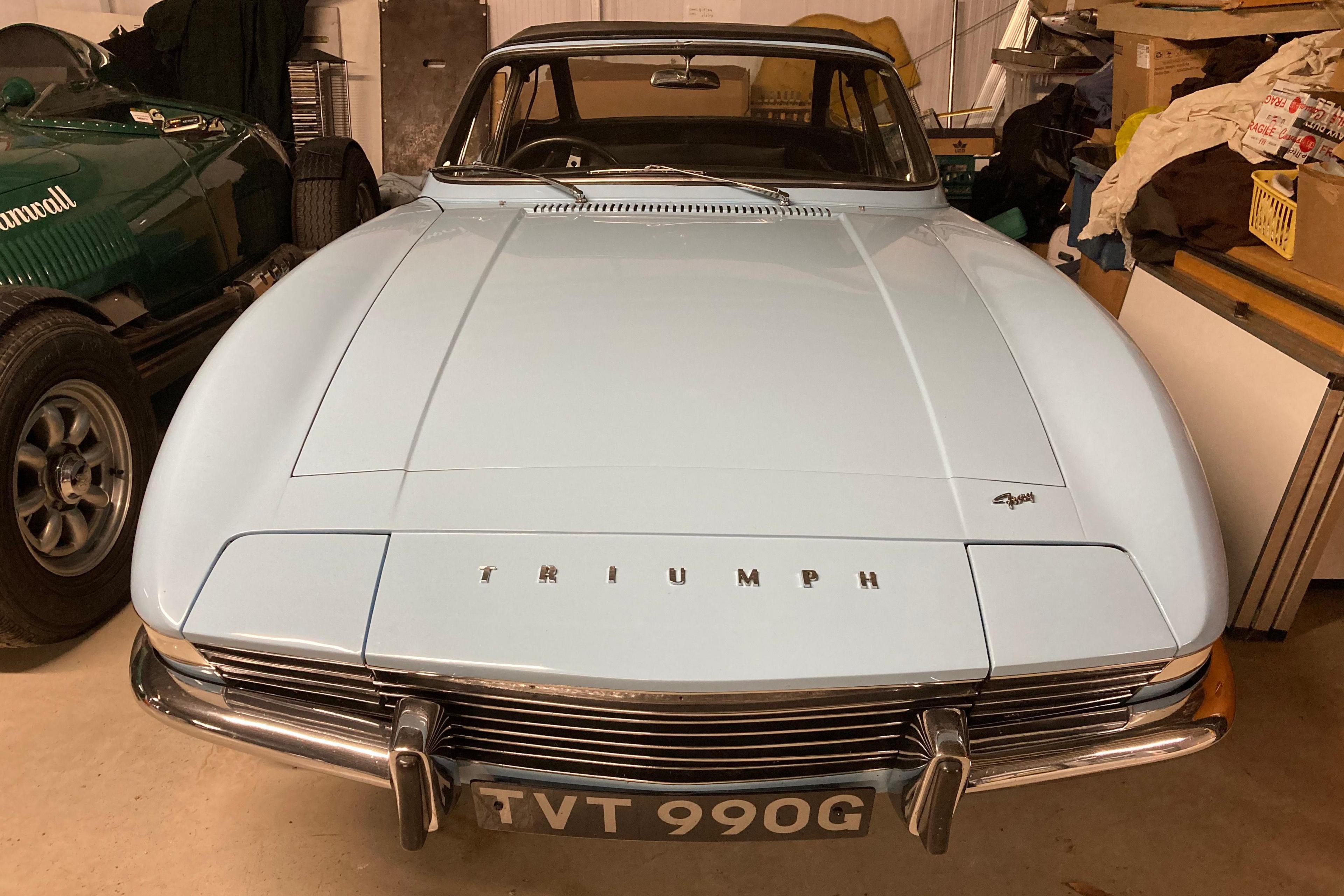 A pale blue sports car with "TRIUMPH" emblazoned across its bonnet.