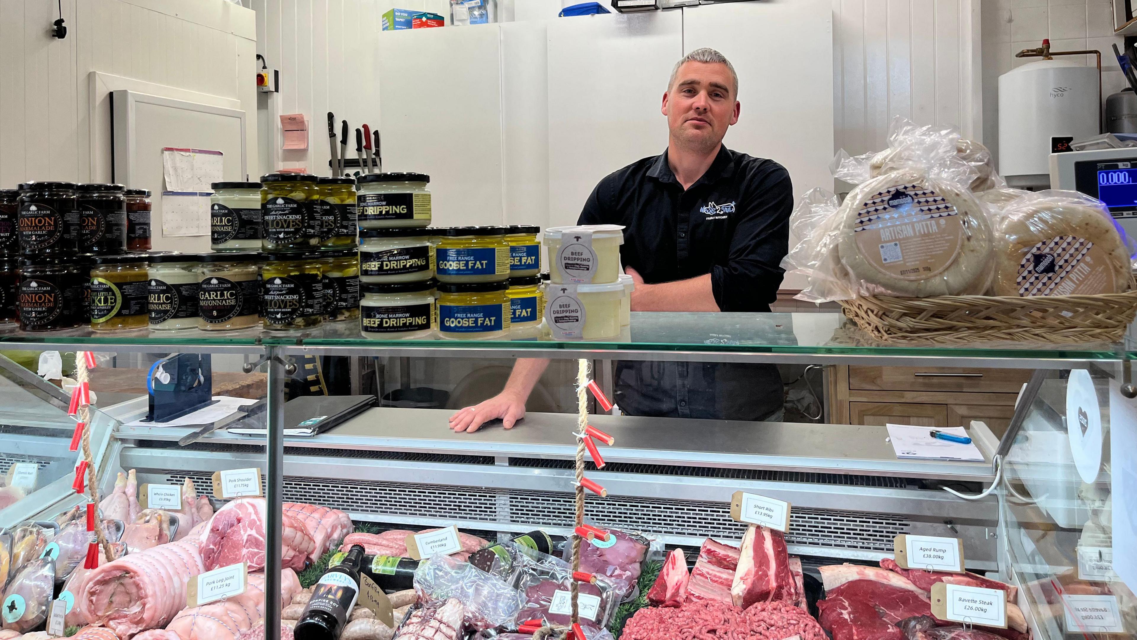 A man in a black shirt is standing behind a butcher's counter.