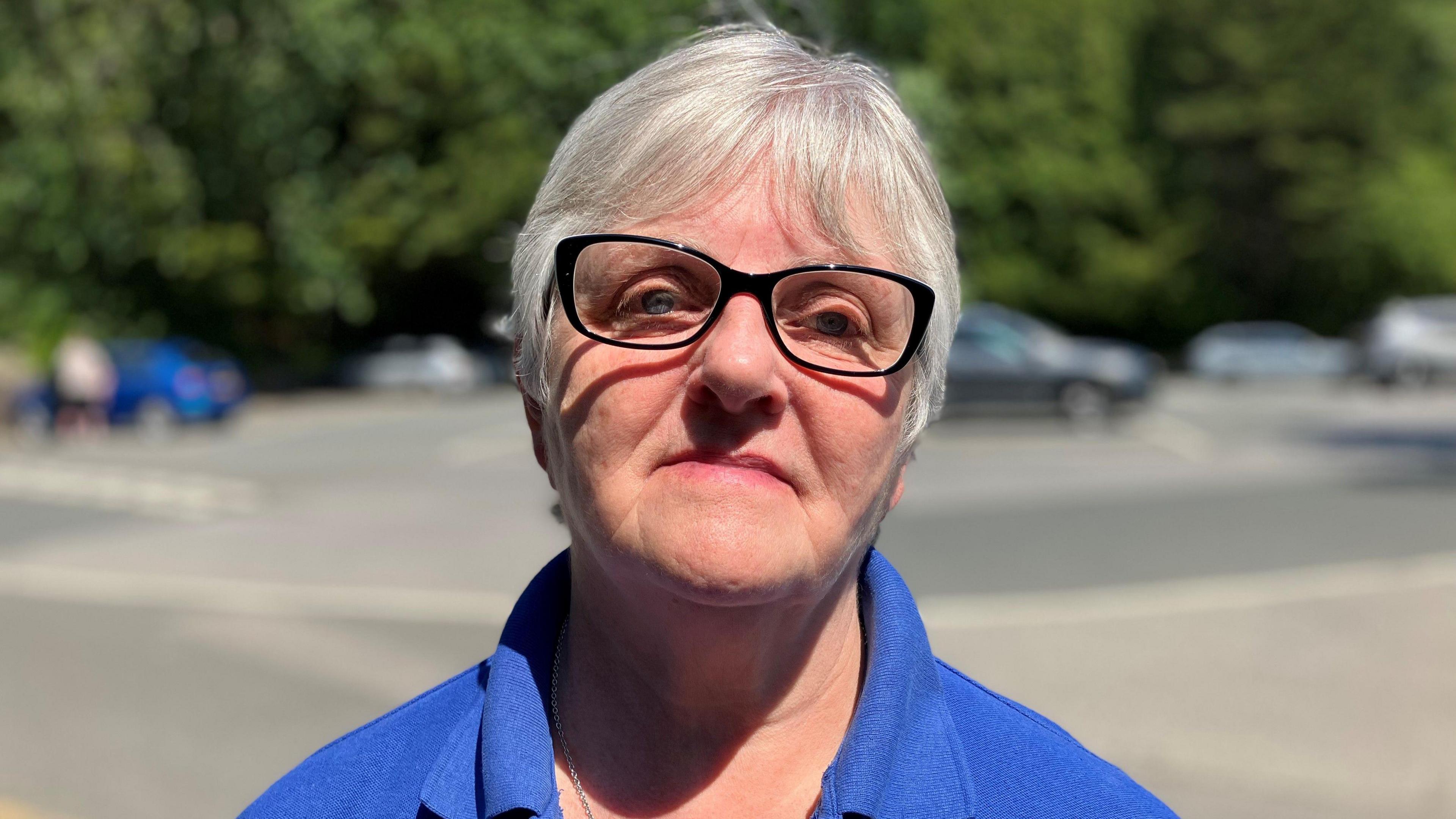 Woman with grey hair and black framed glasses looking unhappy