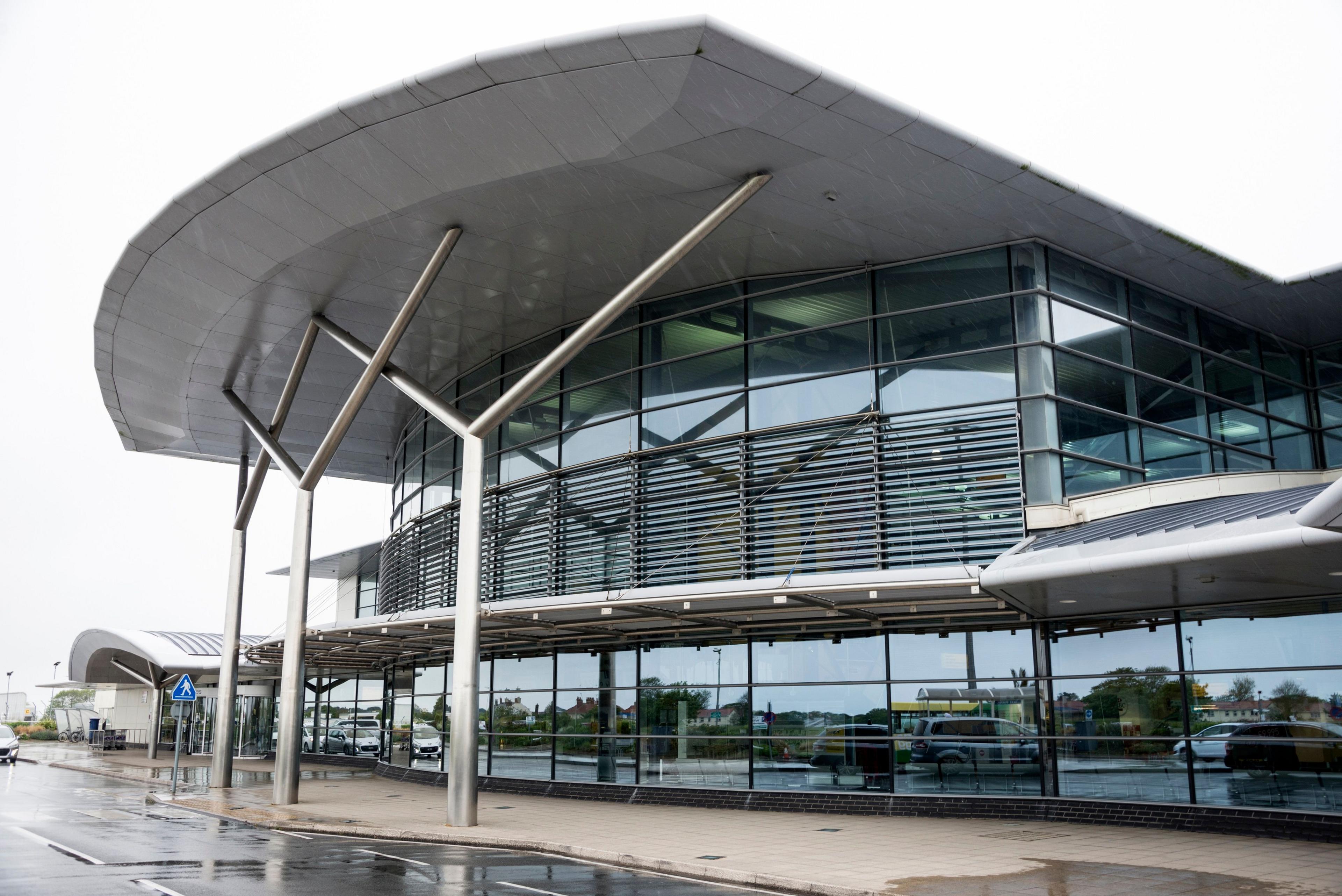 Exterior view of a part of Guernsey Airport showing a glass-fronted building with vehicles reflected in the windows