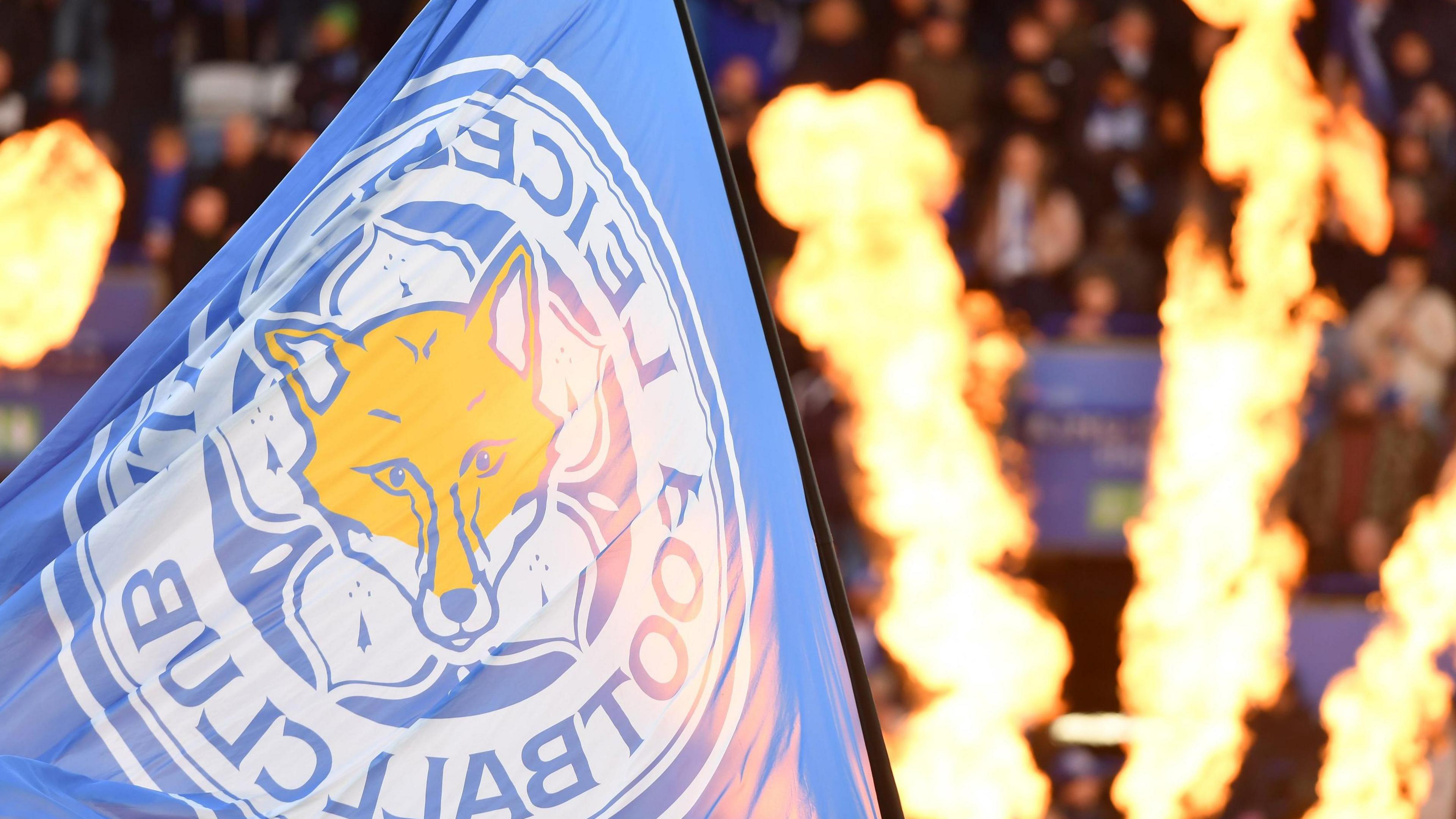 A flag with Leicester City's logo being waved, with pyrotechnic flames in the background