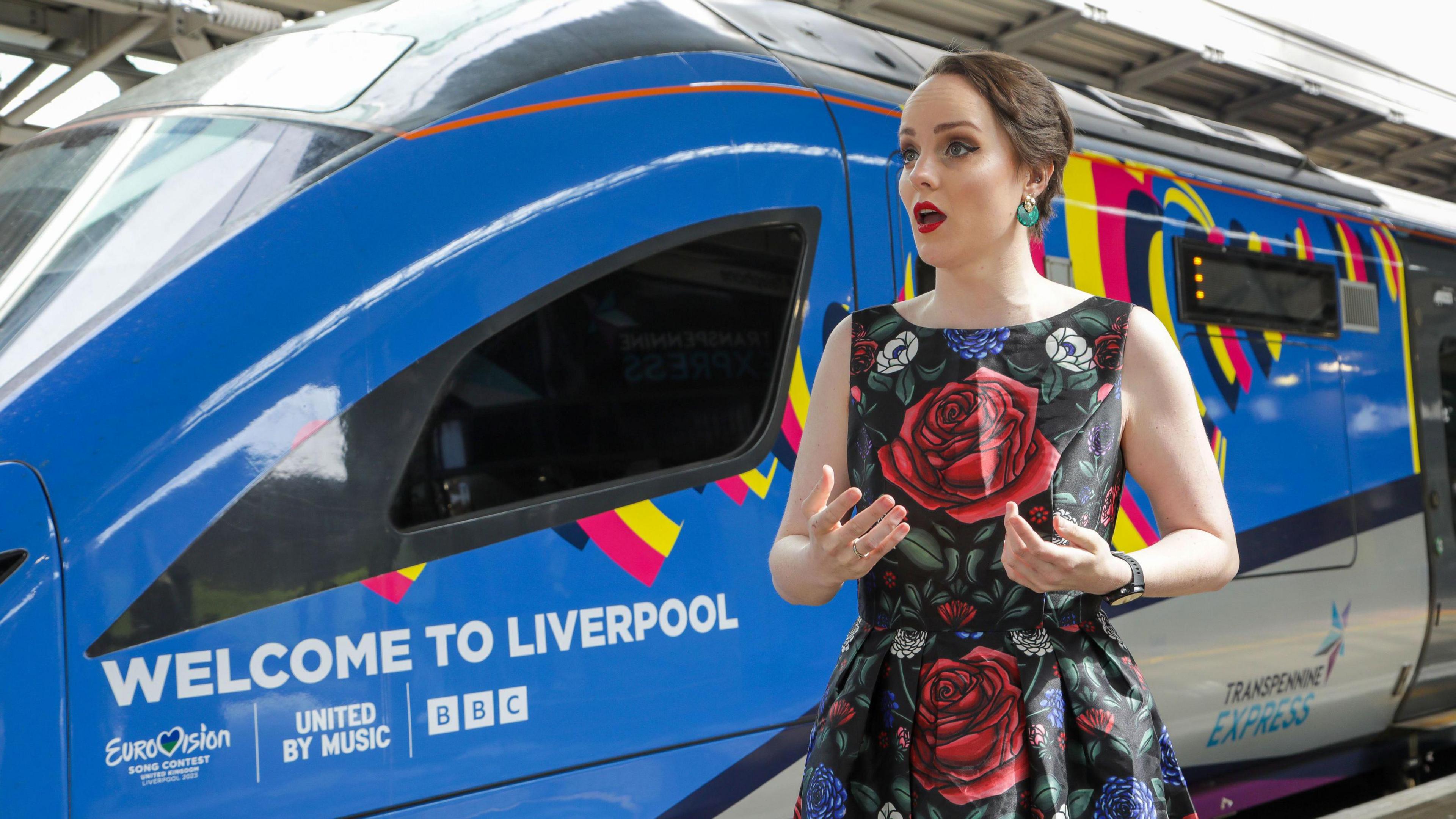 Soprano Morgan Carter in a floral dress bearing roses sings for passengers and railway workers by a TransPennine Express carriage decked in a special Eurovision livery.