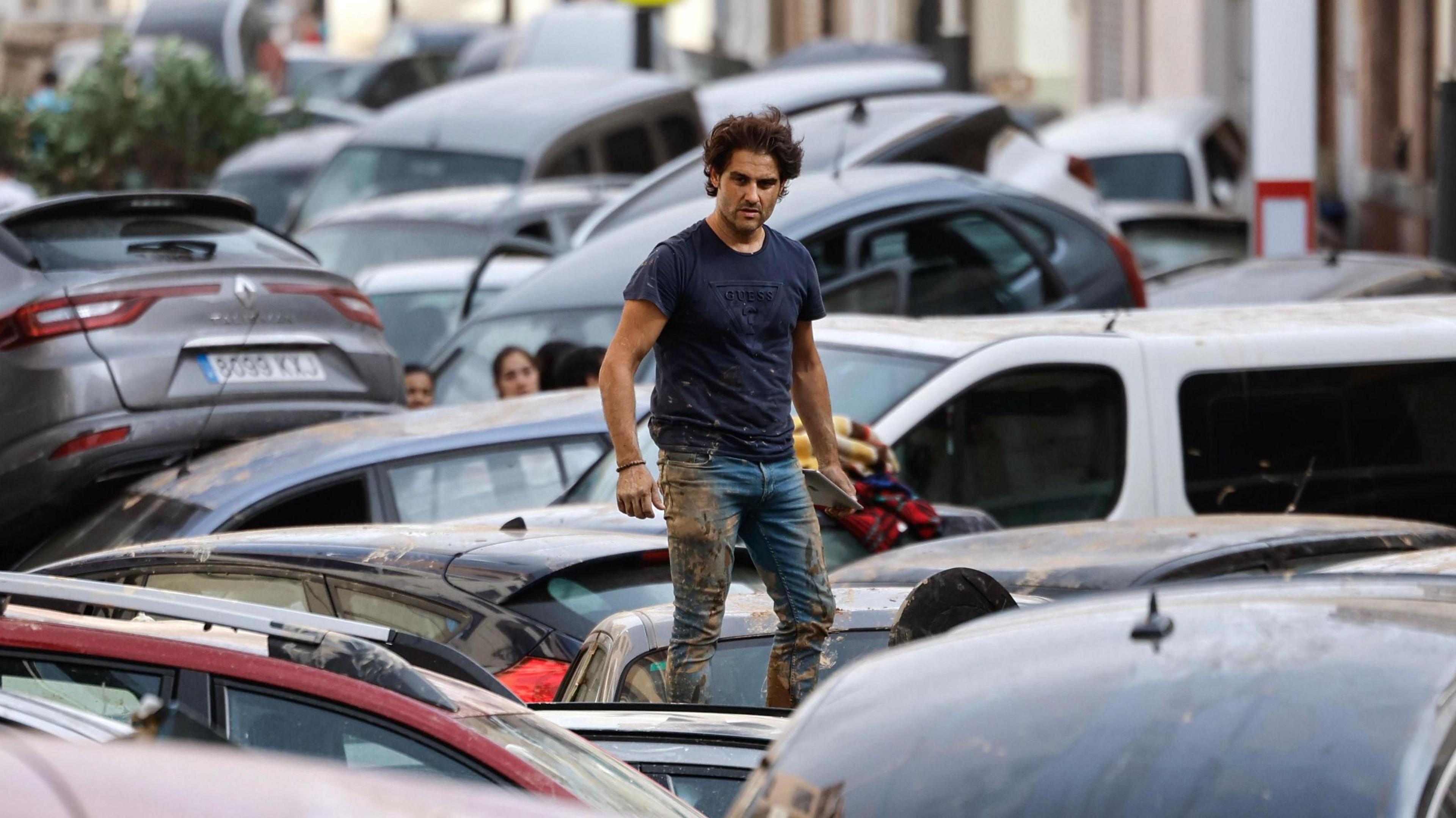 A man wearing mud-stained clothing stands on a pile of cars swept down a road by flood waters in Valencia, in Spain in November 2024