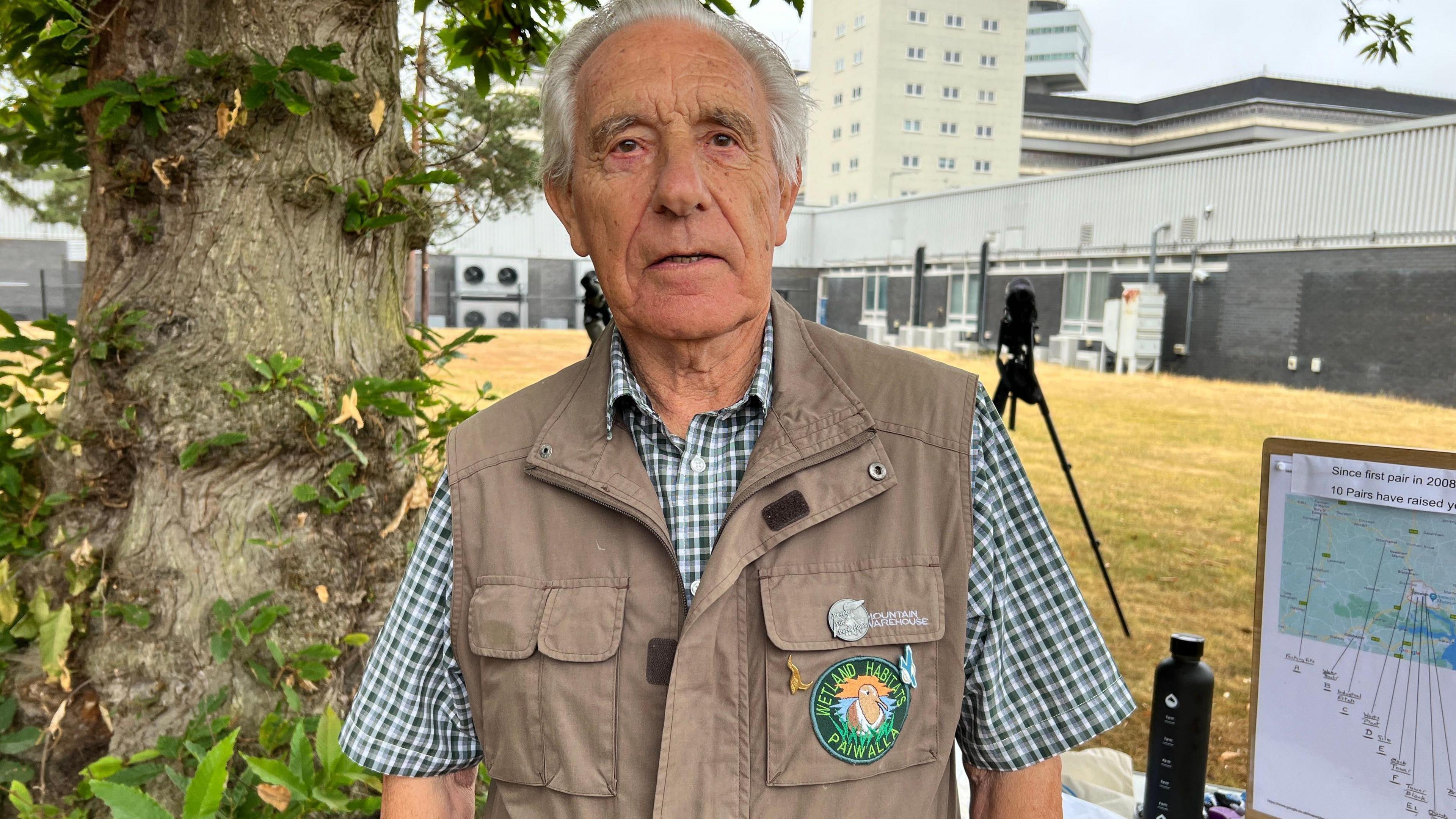 Peter Merchant stands outside by a tree with a tall building in the background