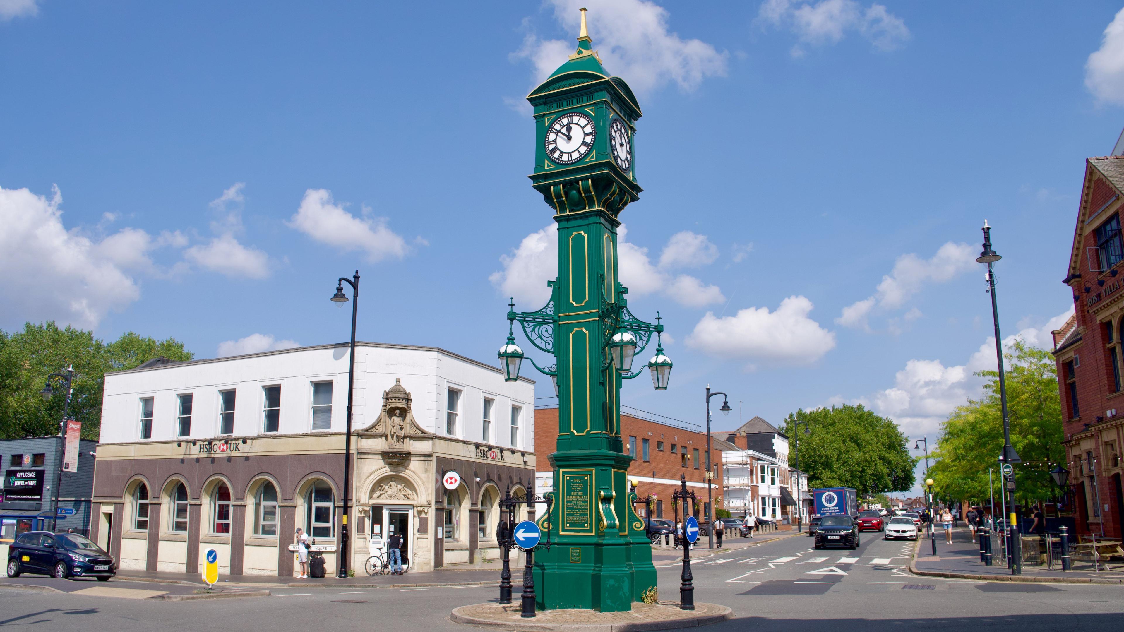 A green clock tower on a road traffic island