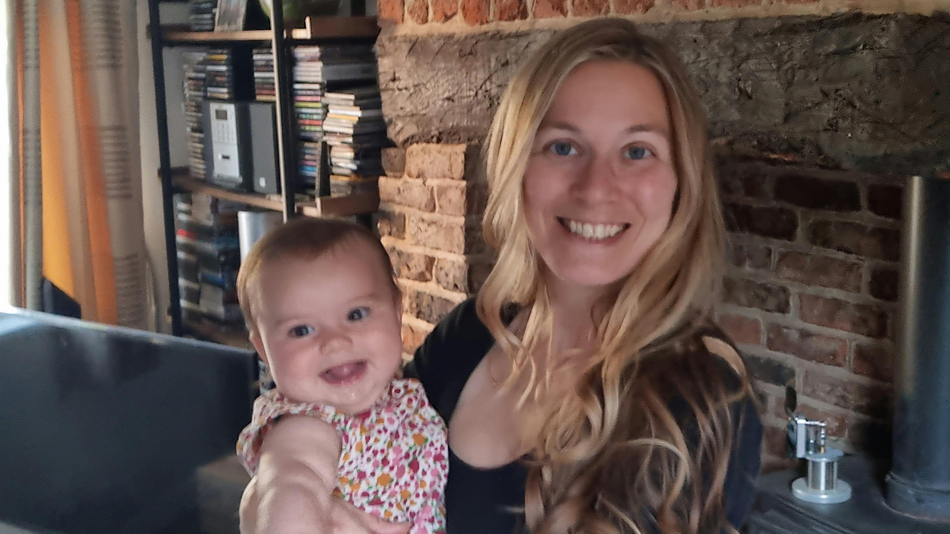 A woman with long blonde hair holding a baby smiling. 