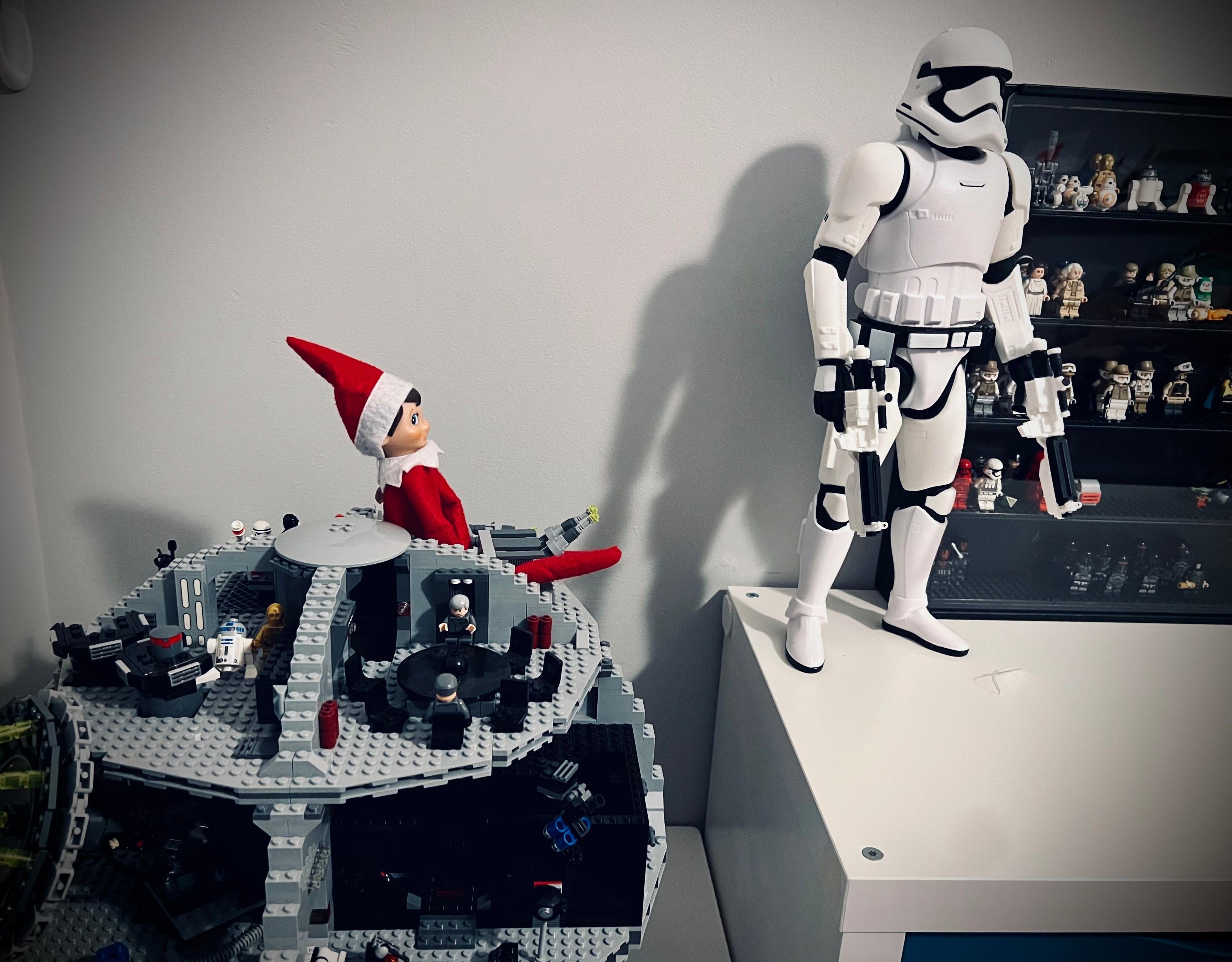 An elf sat on a Lego Death Star looking at a Star Wars stormtrooper. 