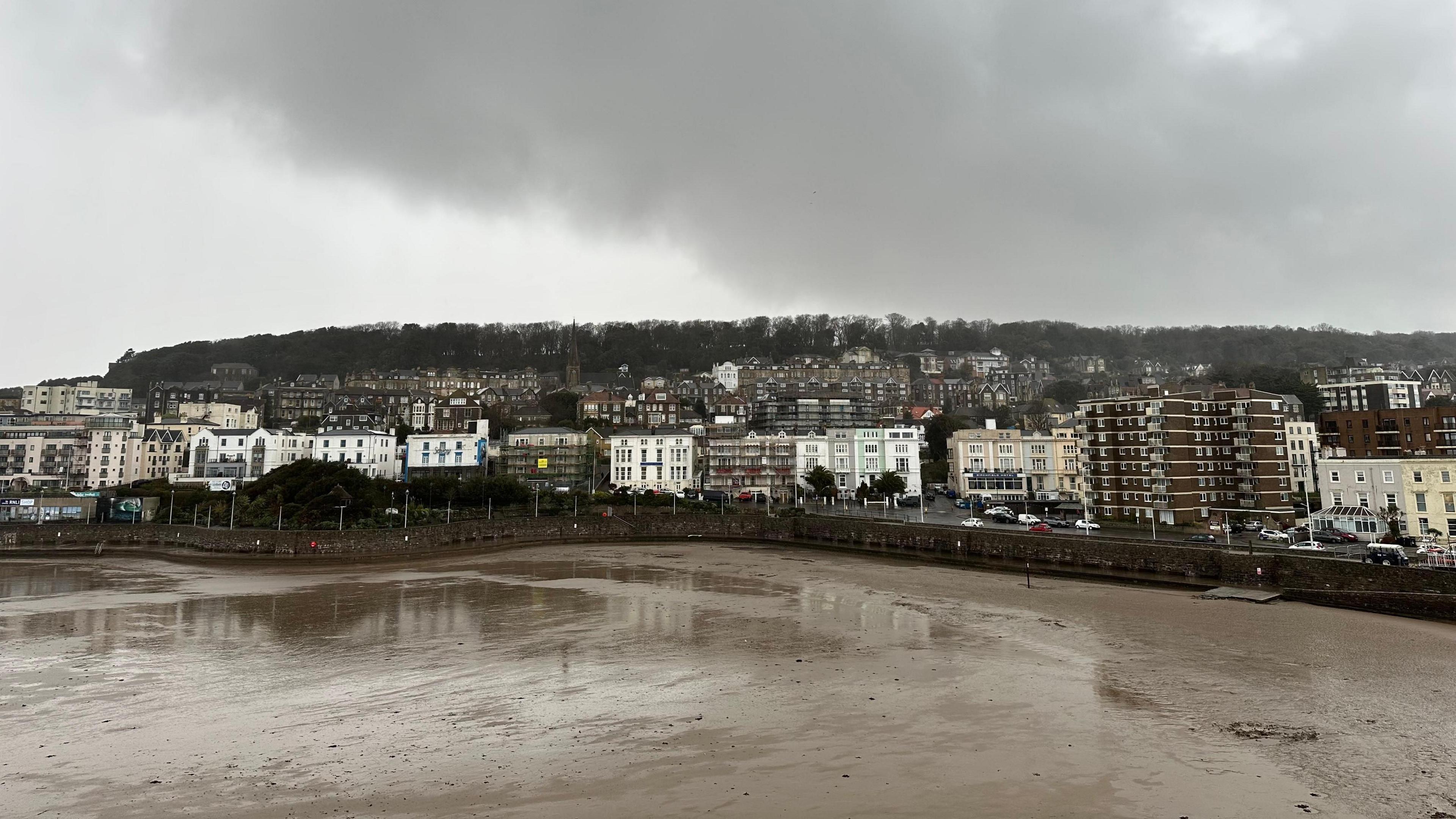 A view of Weston-super-Mare's coast from the beach. Houses are set against a backdrop of a grey, stormy sky.