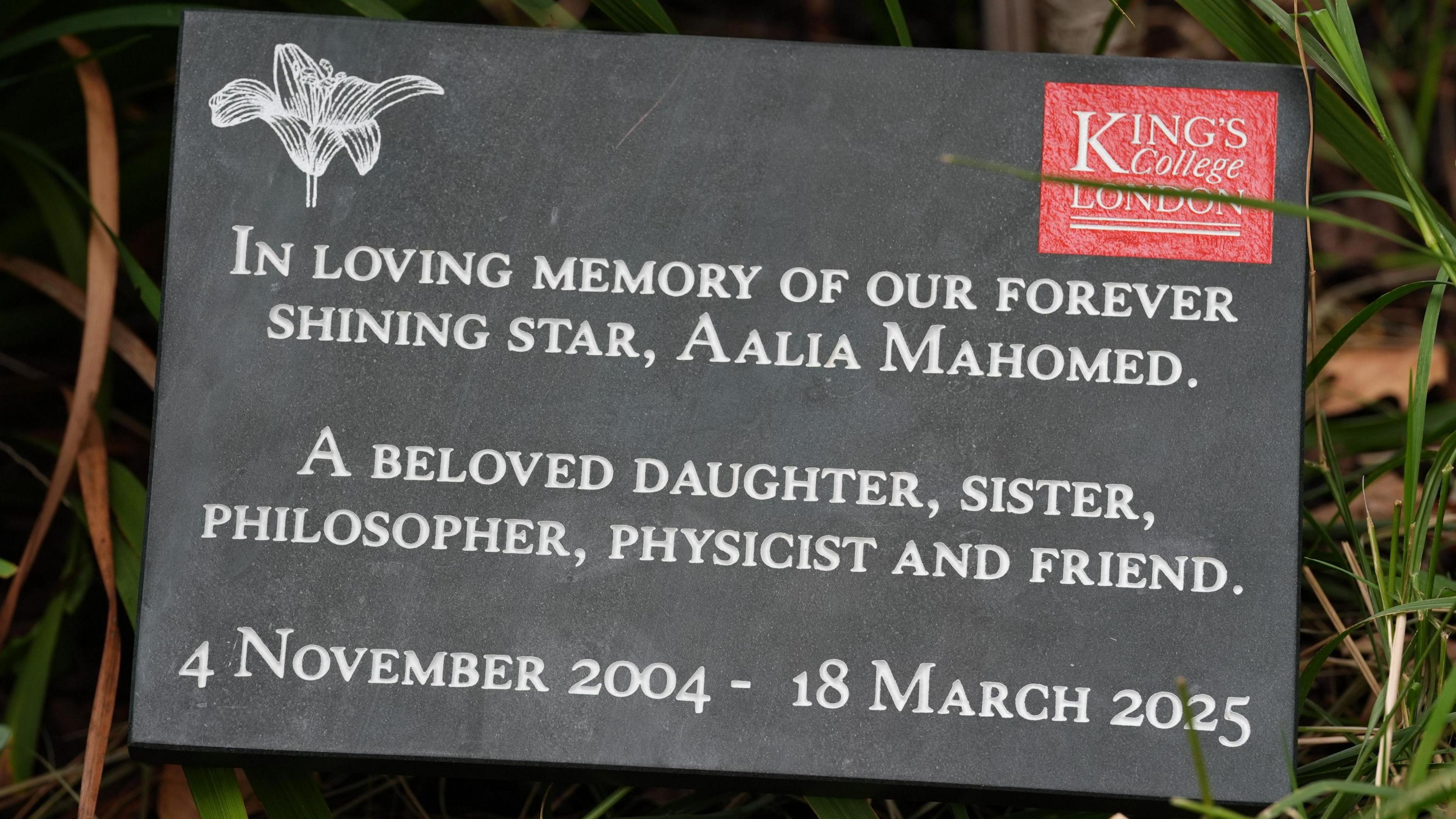 A memorial plaque set in a grassy area, commemorating Aalia Mahomed. It describes her as a cherished daughter, sister, philosopher, physicist, and friend, with her birth and death dates, and includes the King's College London logo in the top right corner.