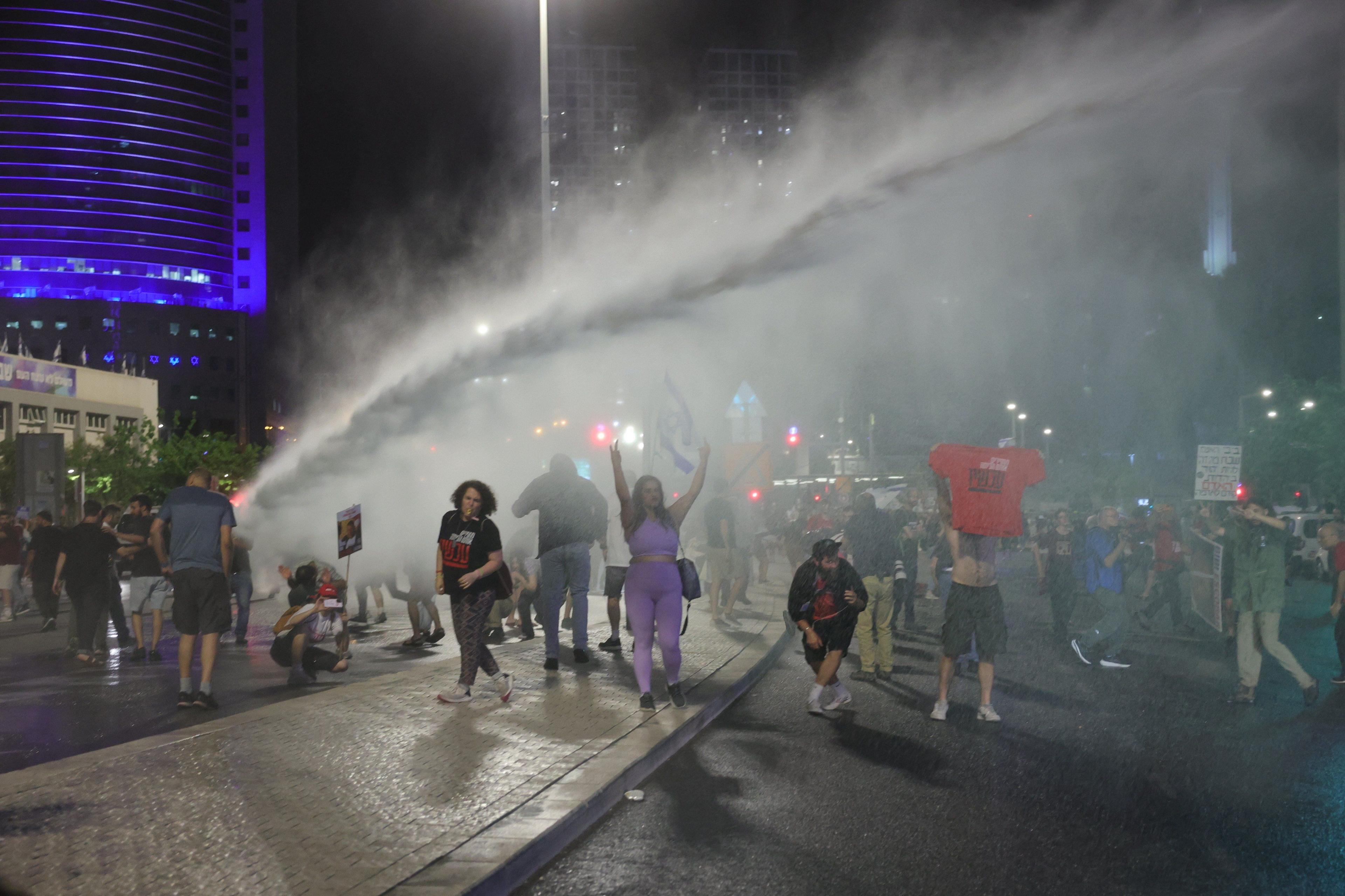 Dozens of protesters on a street in Tel Aviv getting sprayed with water