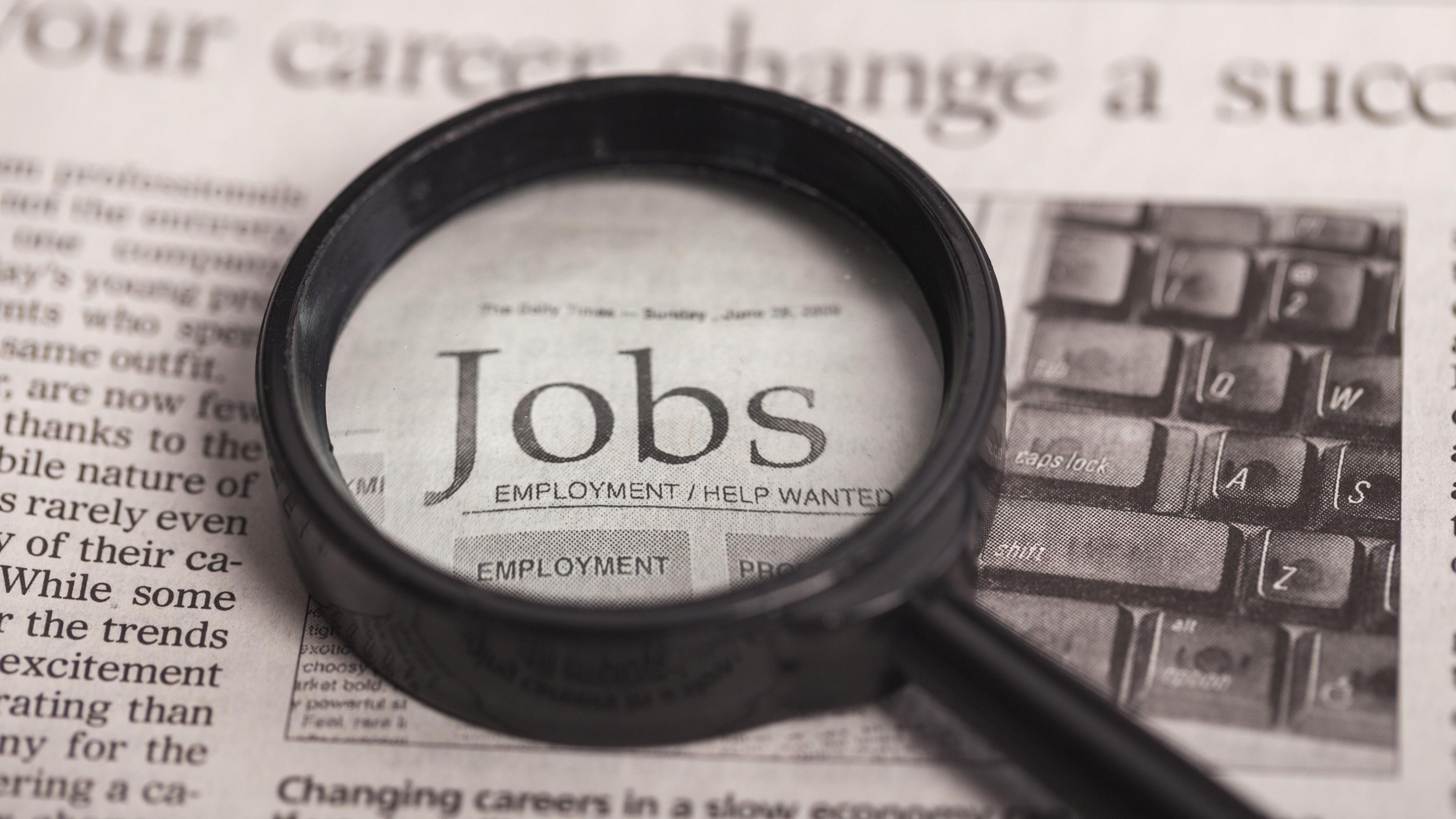 Job advertisement section of a newspaper. A magnifying glass is placed pver the word jobs. 