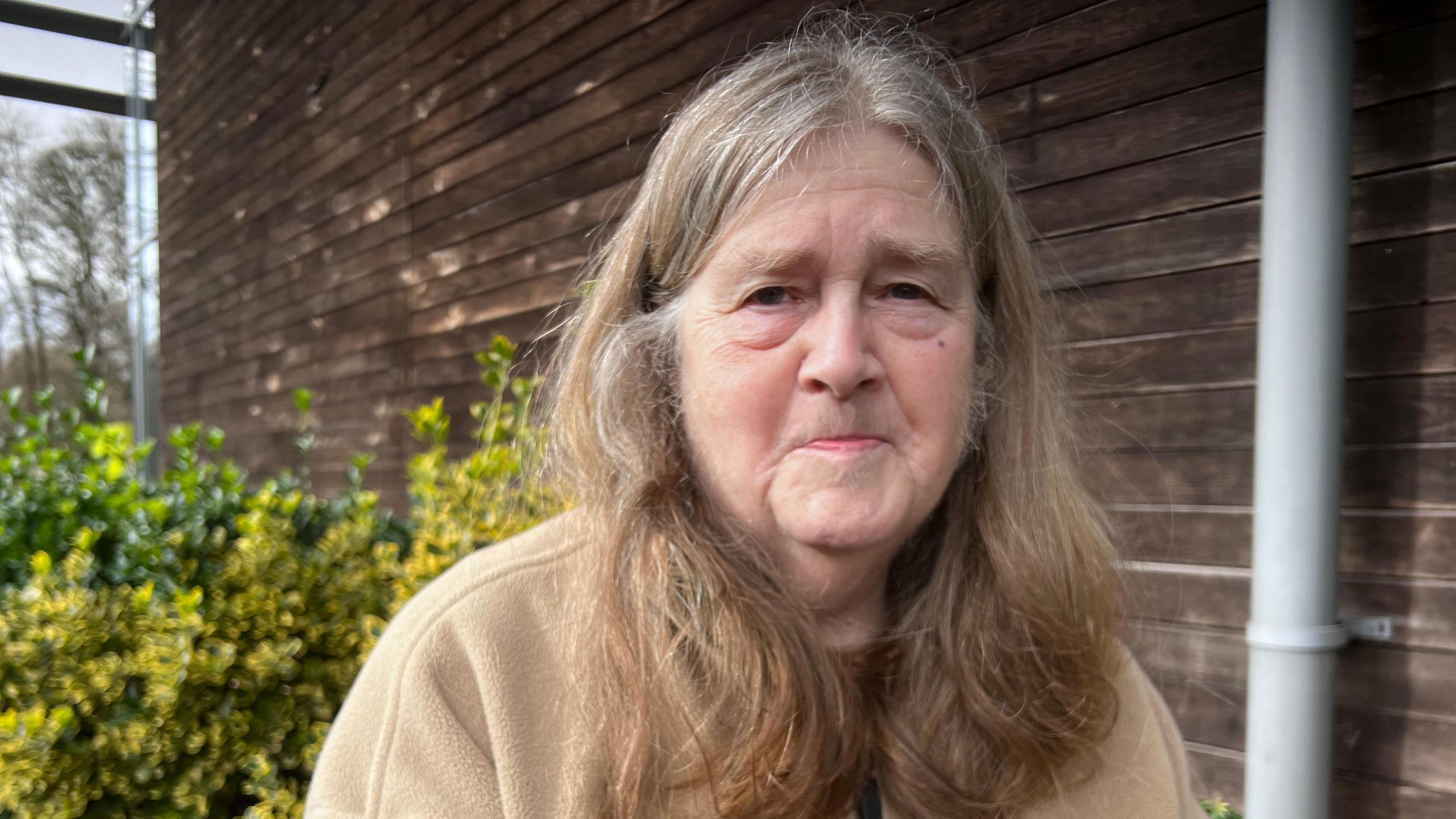 A woman in her later life with long hair and a beige fleece. 