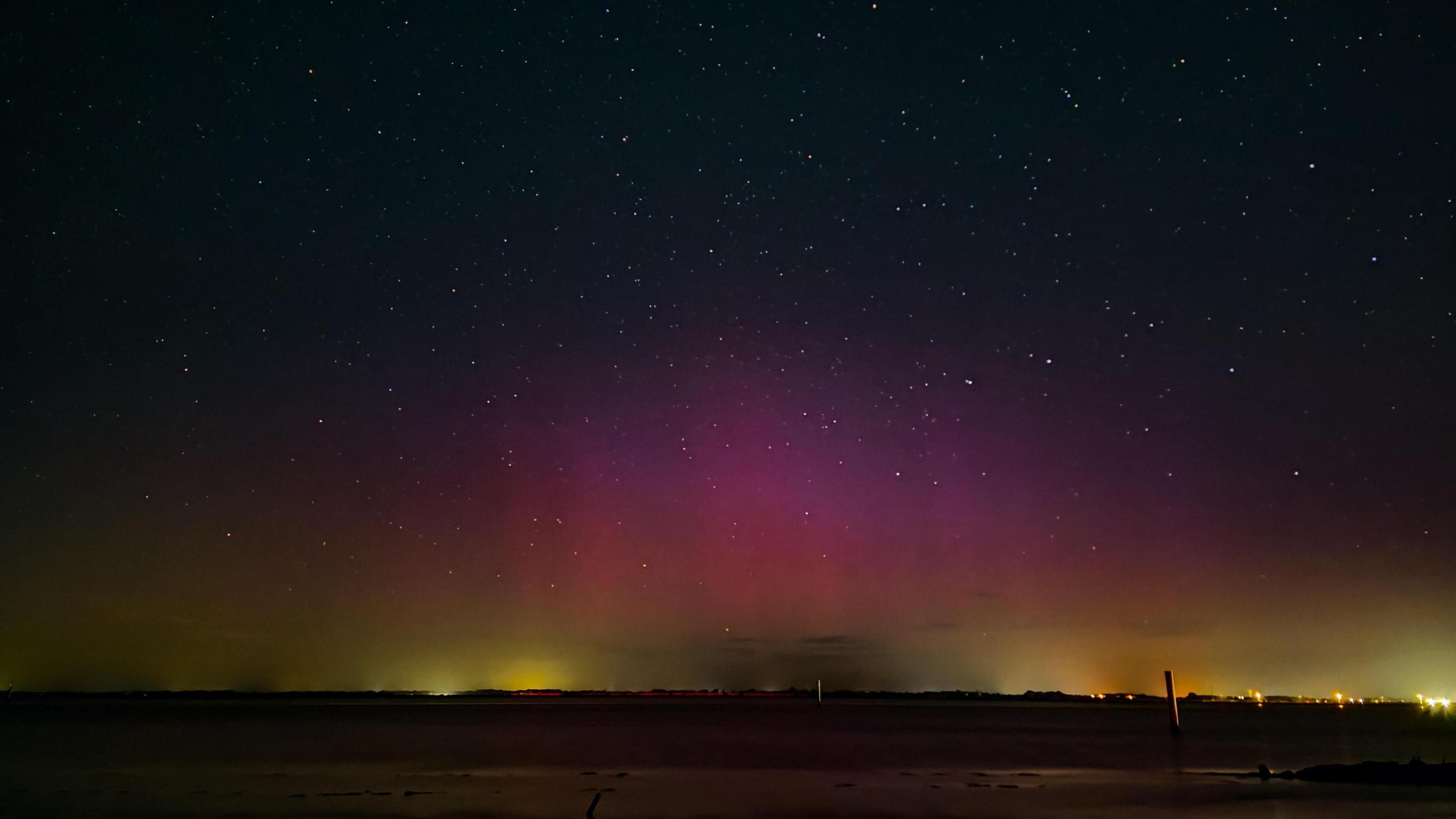 A dark sky is lit in yellow near the horizon, rising to a striking red and pink colour