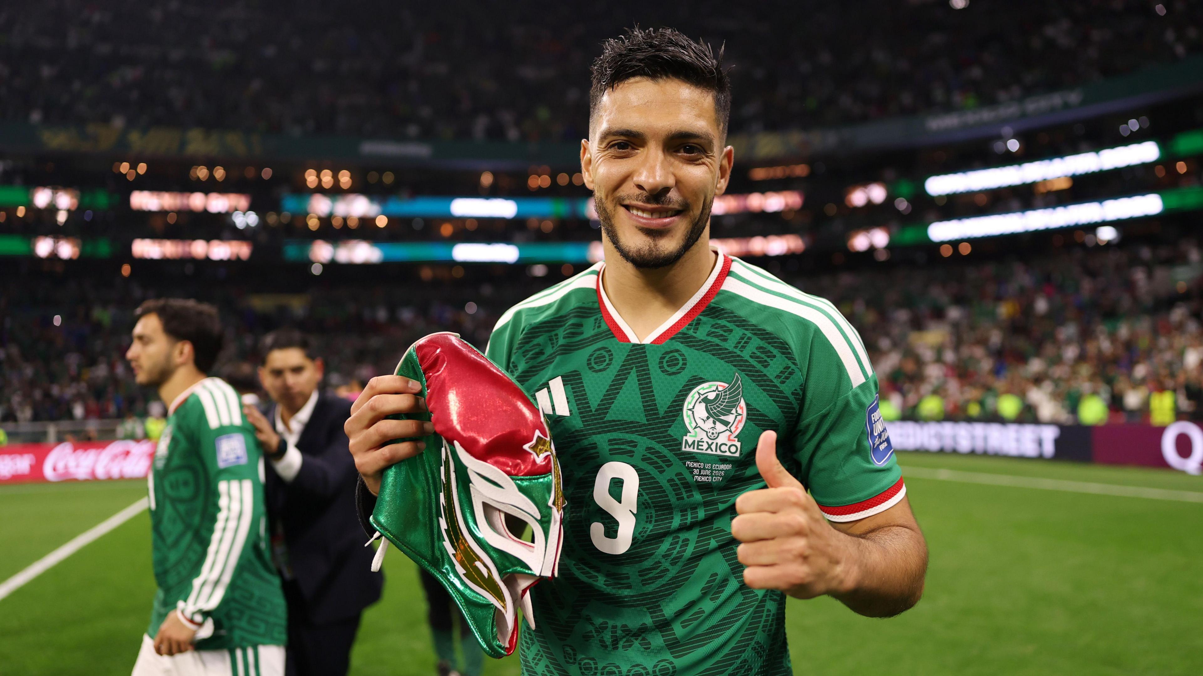 A photo of Raul Jimenez, wearing his green Mexico kit, smiling into the camera as he holds a mask and puts his thumb up after their win against Ecuador on Wednesday