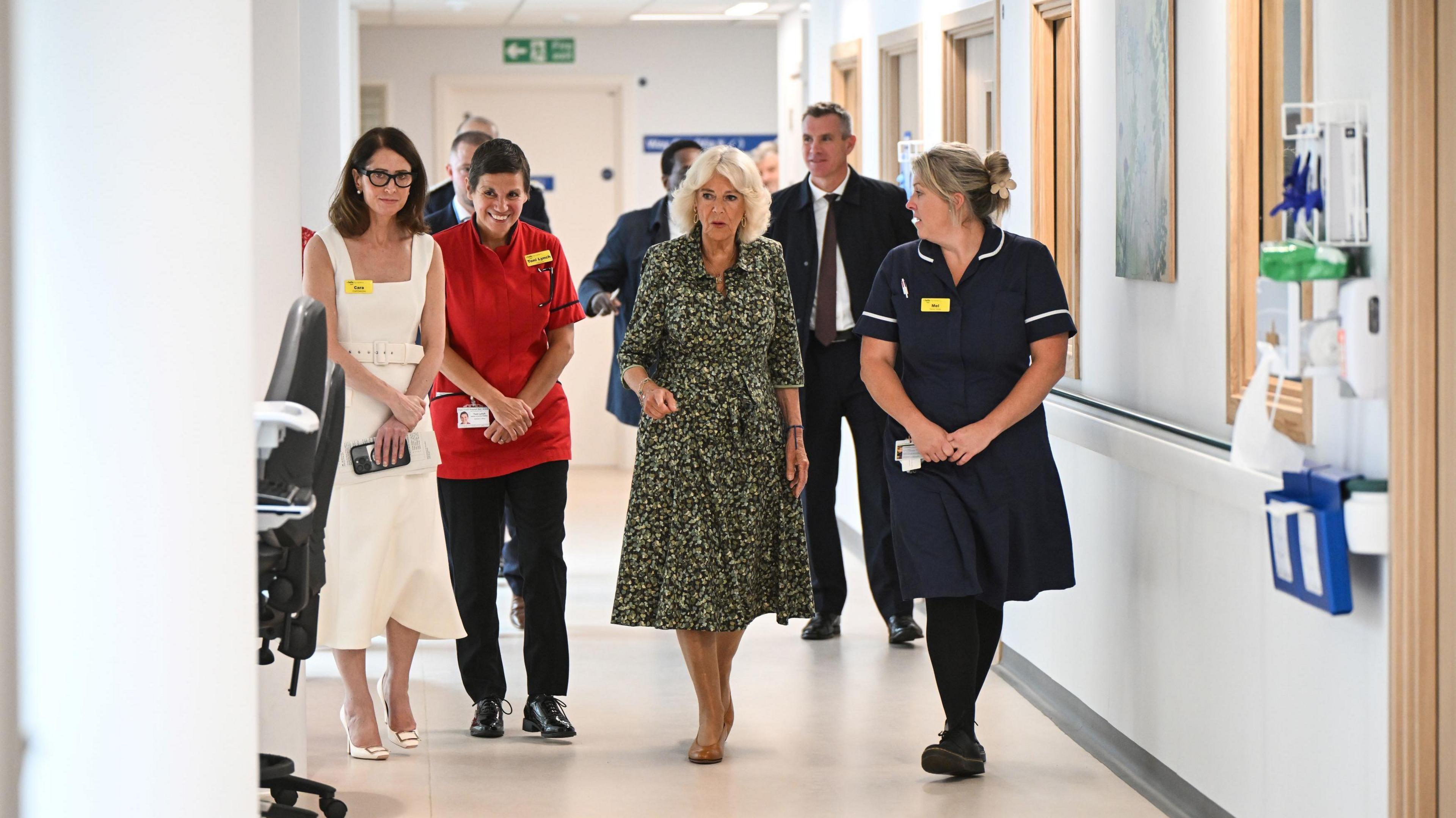 The Queen walking down a clean and light hospital corridor with medical staff