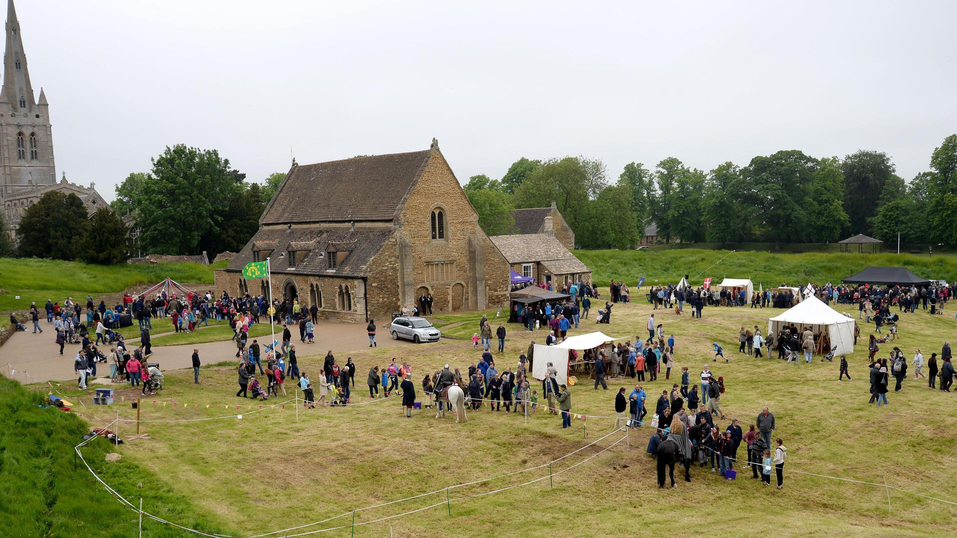 Oakham Castle surrounded by visitors and stalls. A man on horseback can be seen inside a large pen.