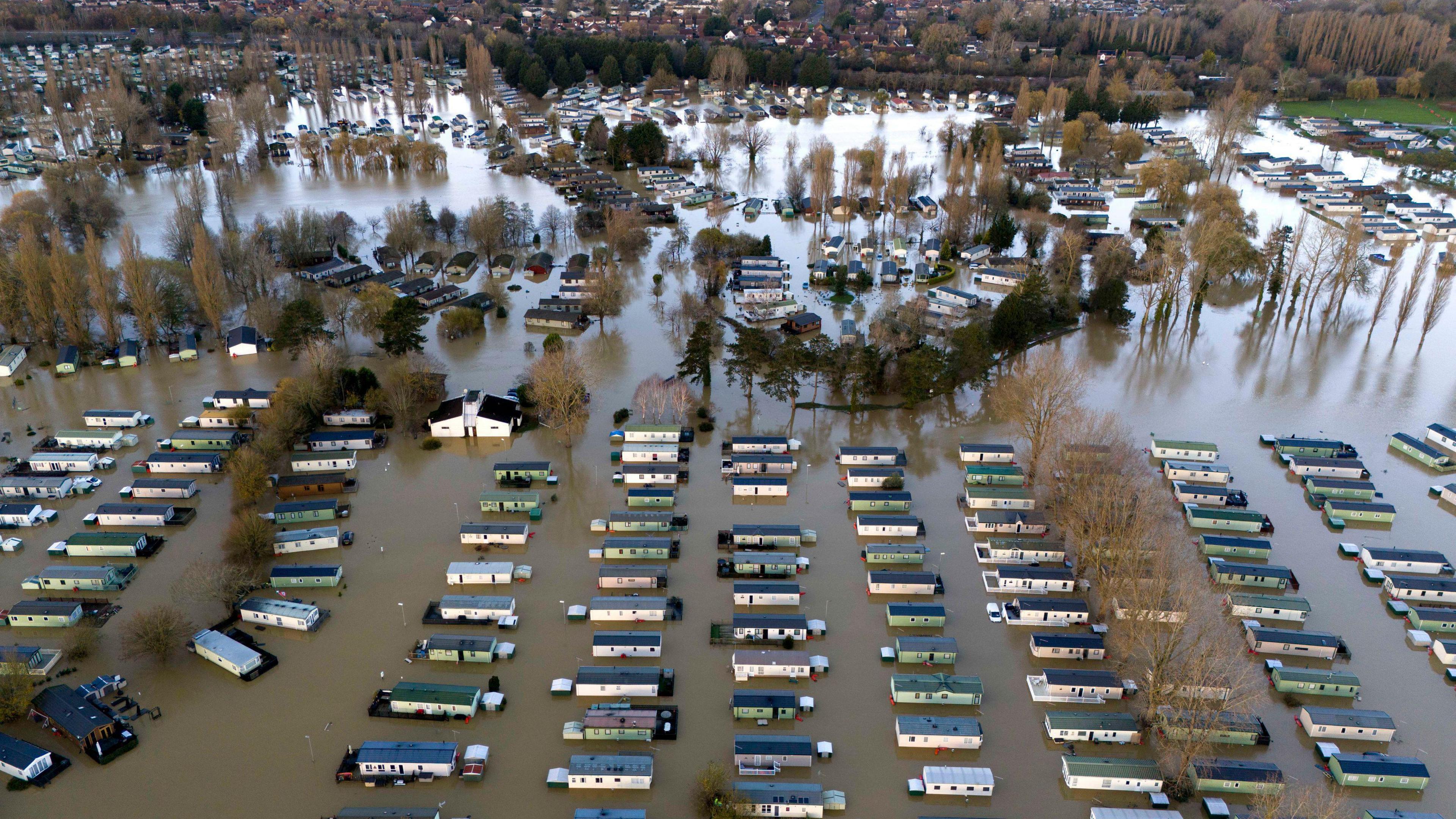 A birds eye view of Billing Aquadrome near Northampton, where dozens of modular homes can be seen partially submerged in flood water. Trees can be seens and houses in the background