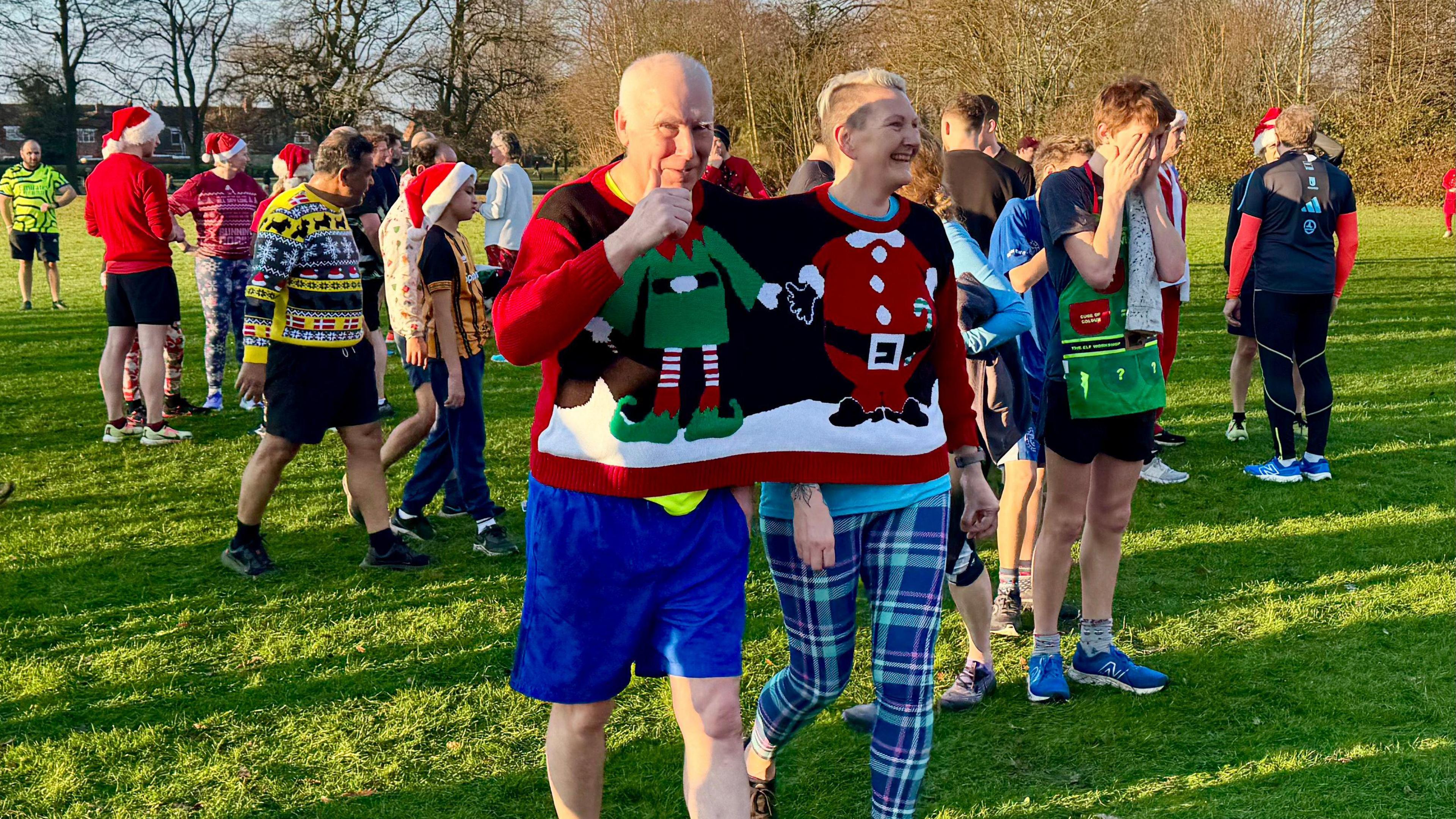 Two people wearing one large festive jumper.