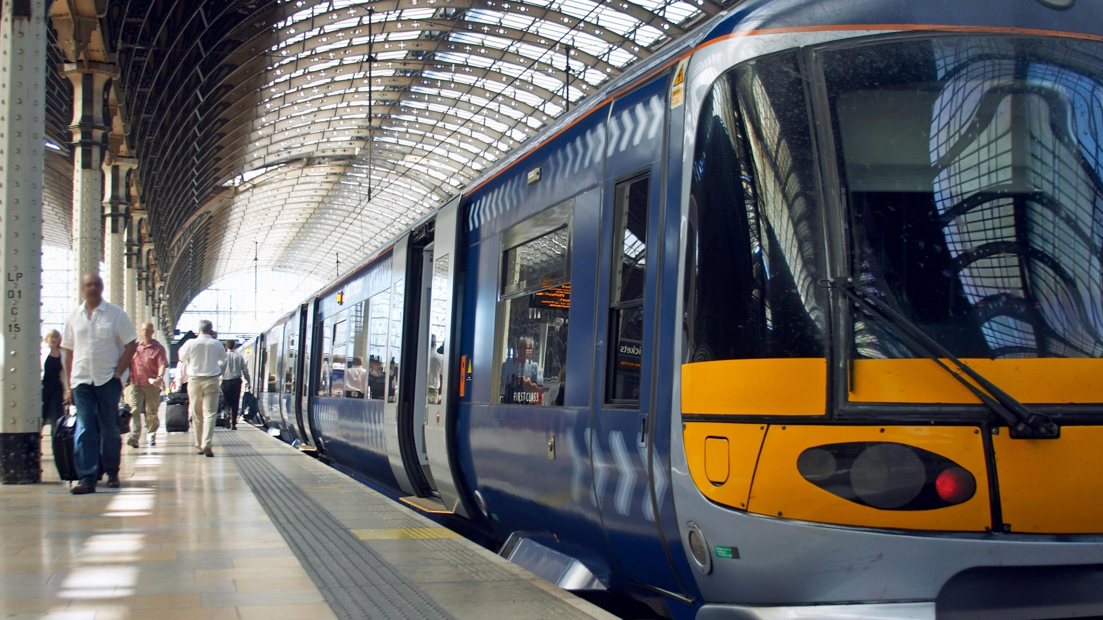 A Southeastern train, in its blue and white livery, stands at a platform under a large glass and iron Victorian station ceiling, with passengers getting on and off the train.