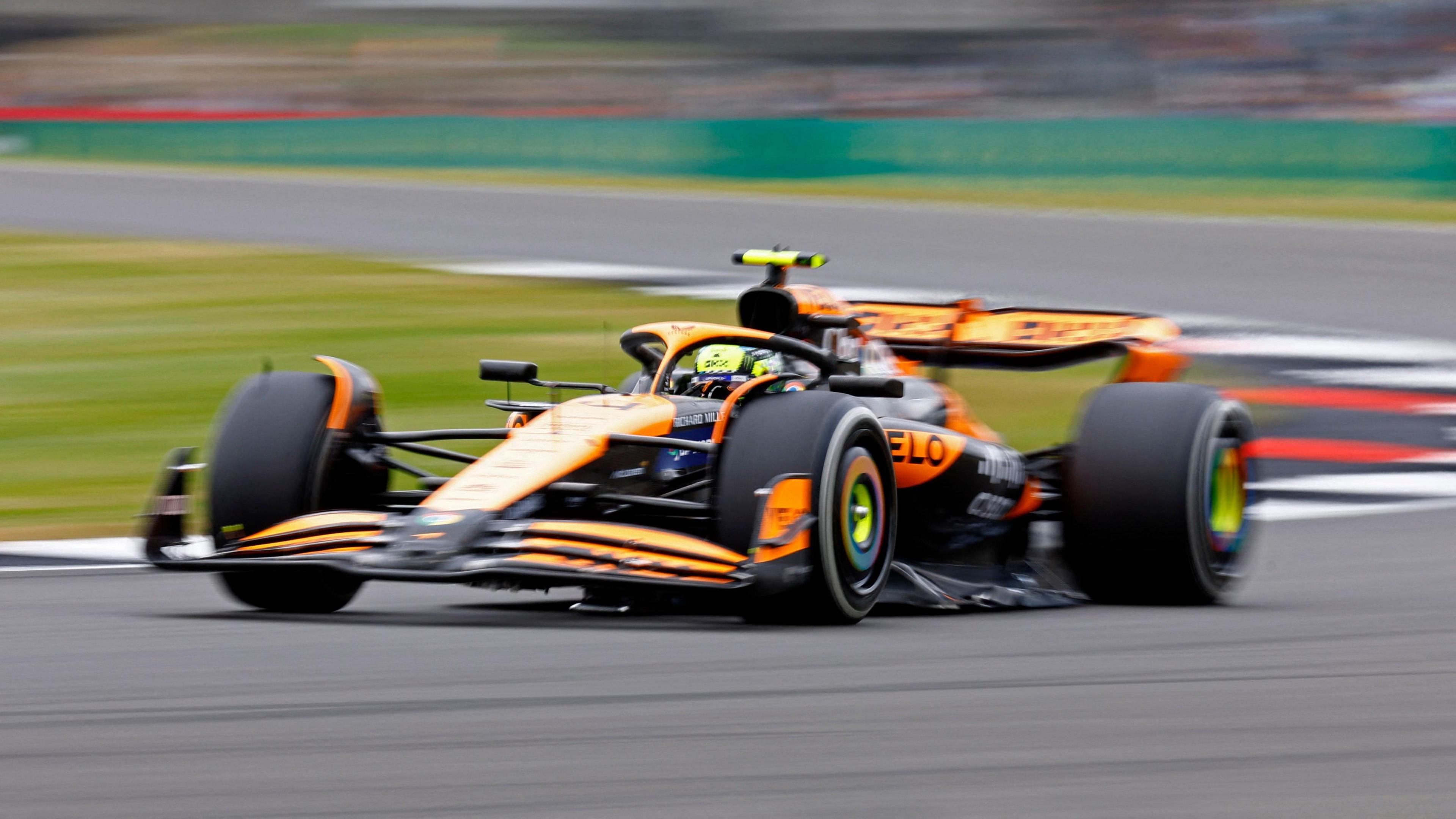 An orange McLaren Formula 1 car whizzes around the track at Silverstone.