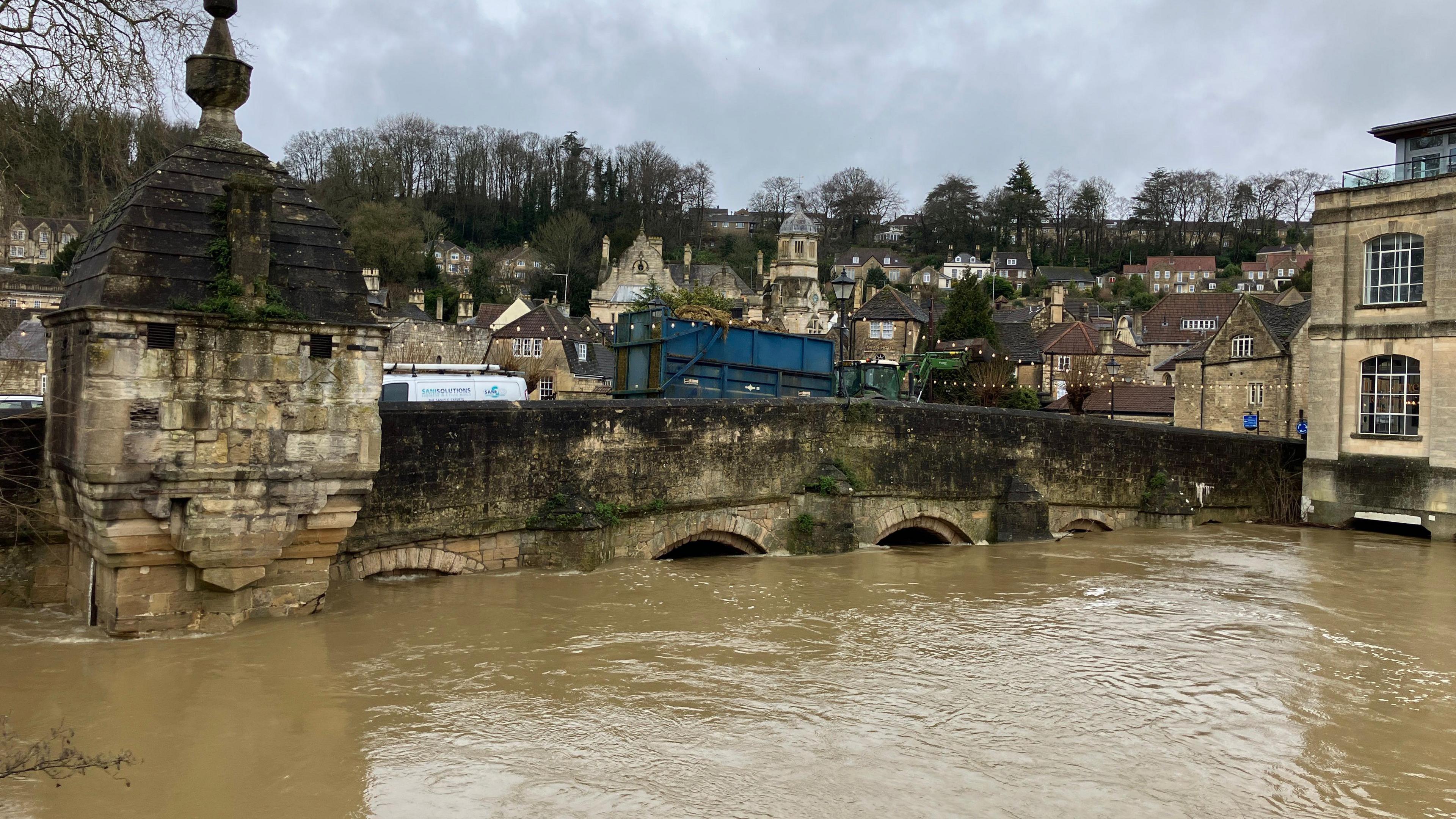 The River Avon's water is high in Bradford-on-Avon in the town centre. The brown water of the river is seen close to the main structure of a stone bridge