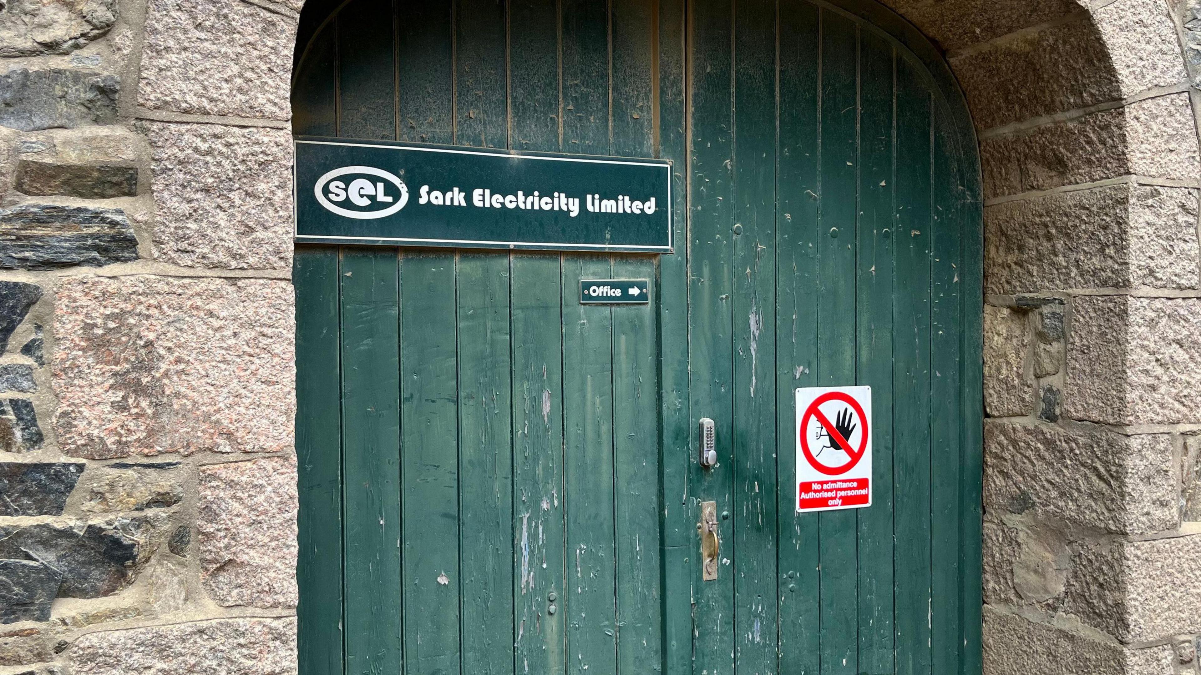 A picture of a green wooden door with the logo for Sark Electricity Limited on it. There is also a No Admitance sign.