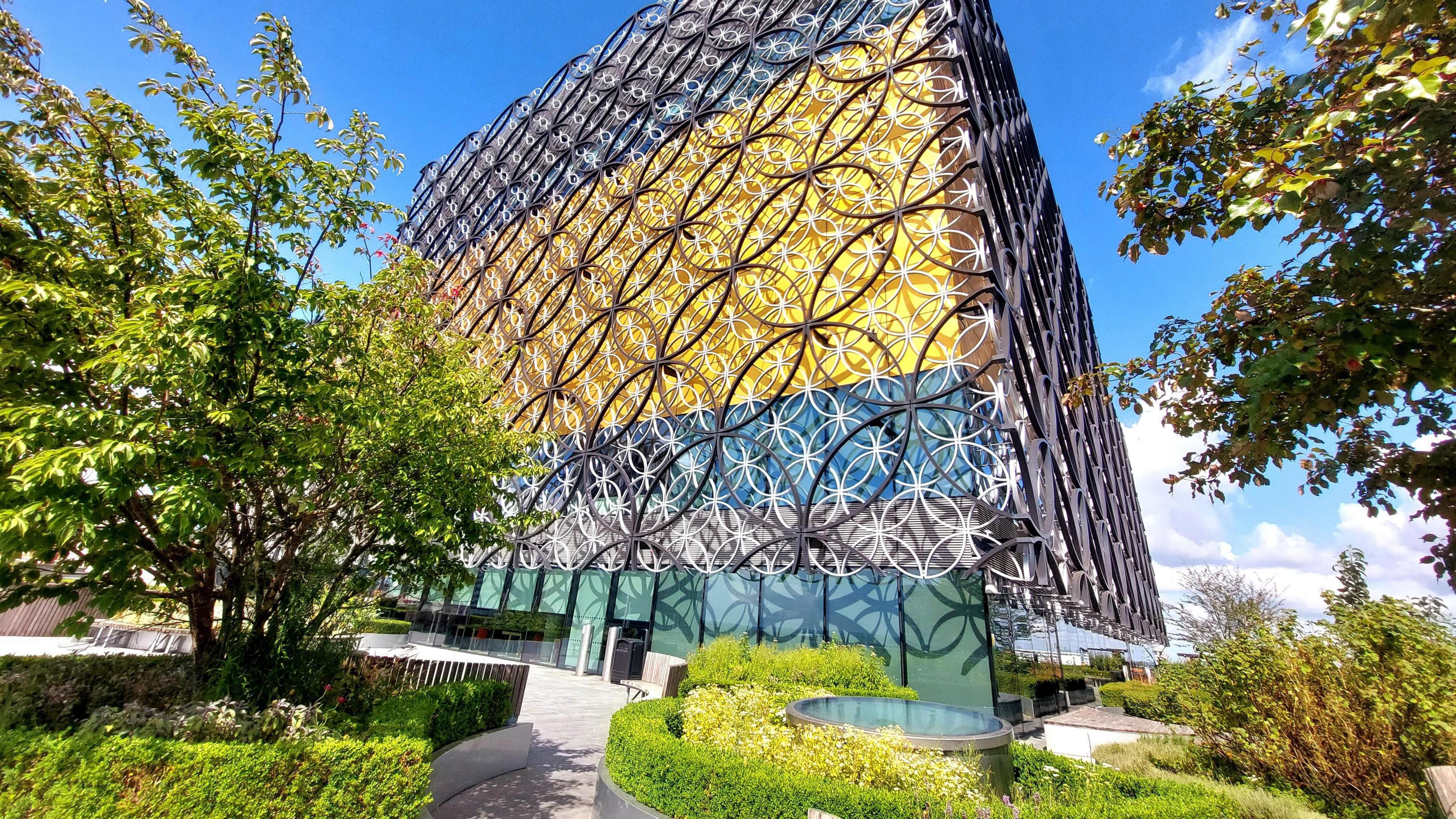 Birmingham Library in the sunshine with green bushes and trees in the foreground 
