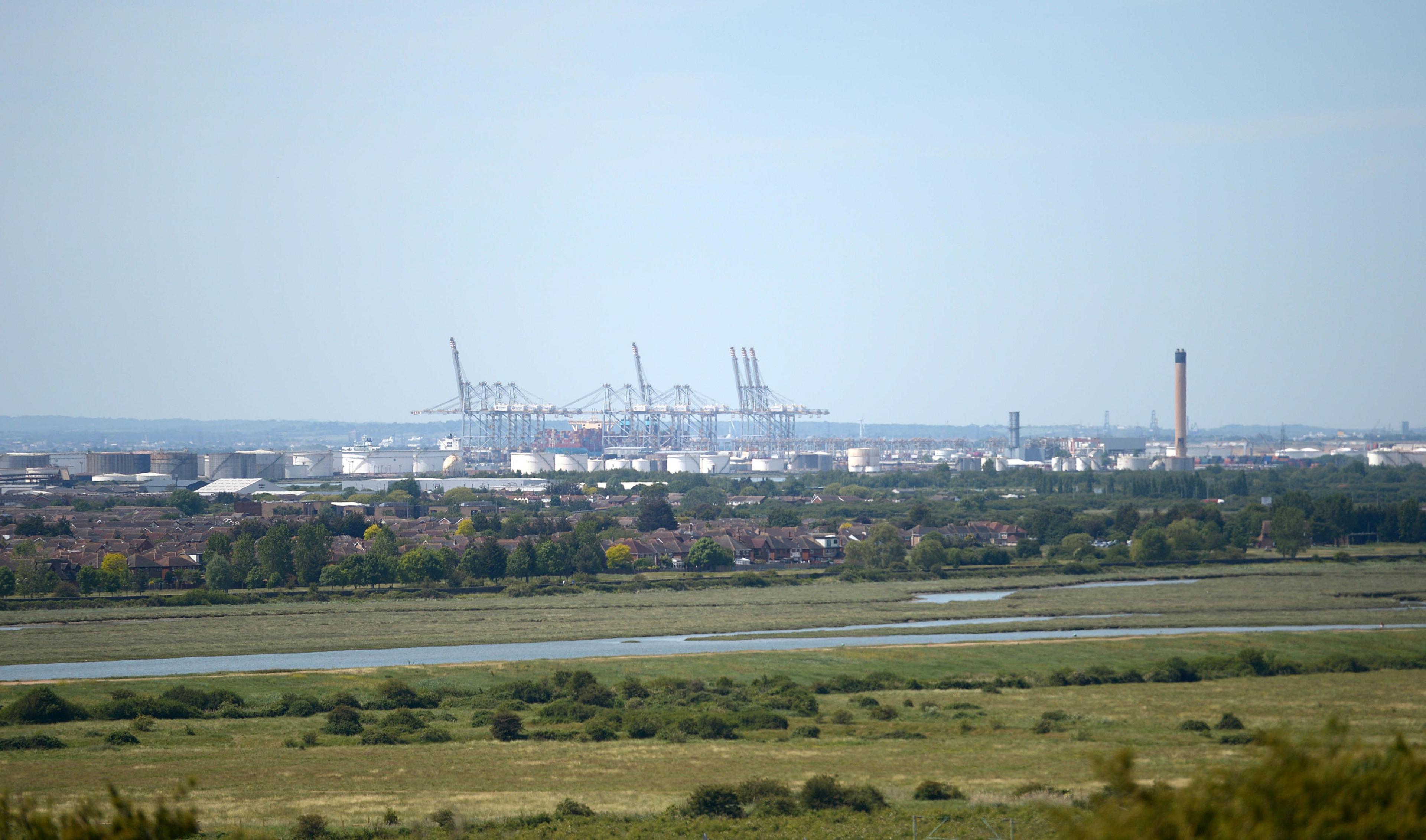 Long range view of the cranes of the Thames Gateway port, with refinery drums, housing and marshland in the foreground