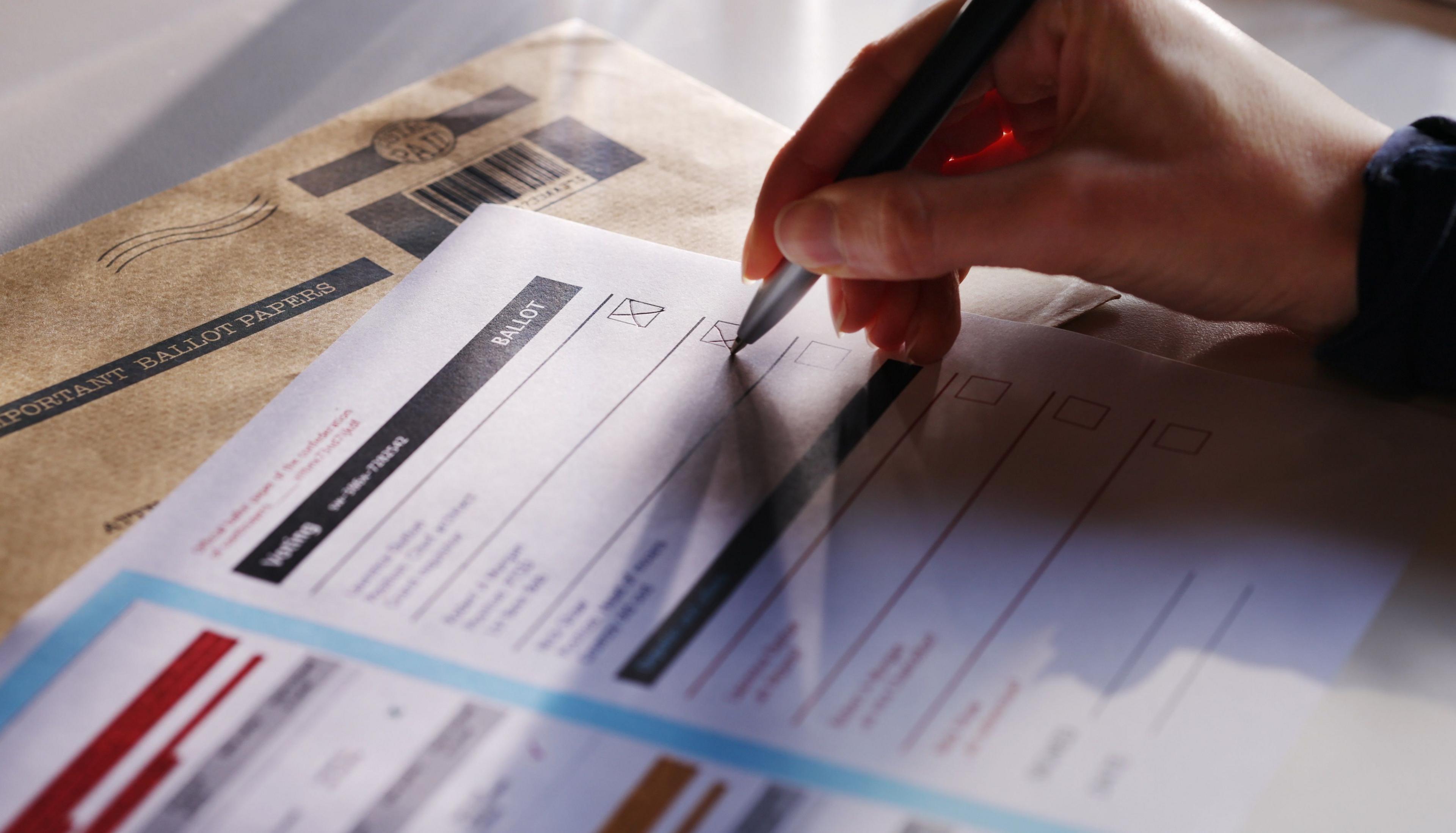 A hand putting a cross on a ballot sheet