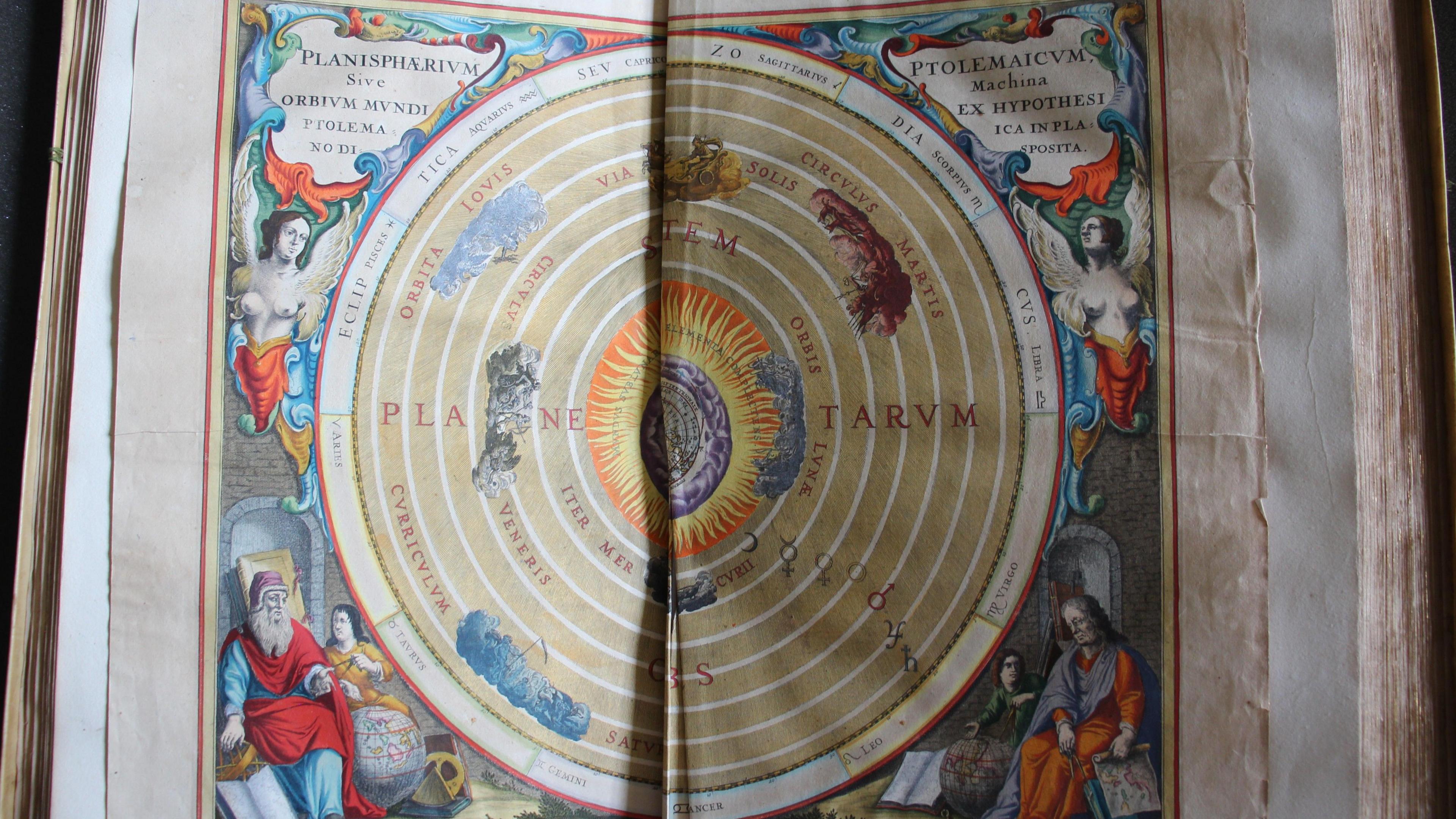 An elaborate and colourful double page illustration of planets in a circular pattern, with Latin descriptions and depictions of biblical and celestial figures in the corners. The pages are coming away in the middle and the edges are tattered.