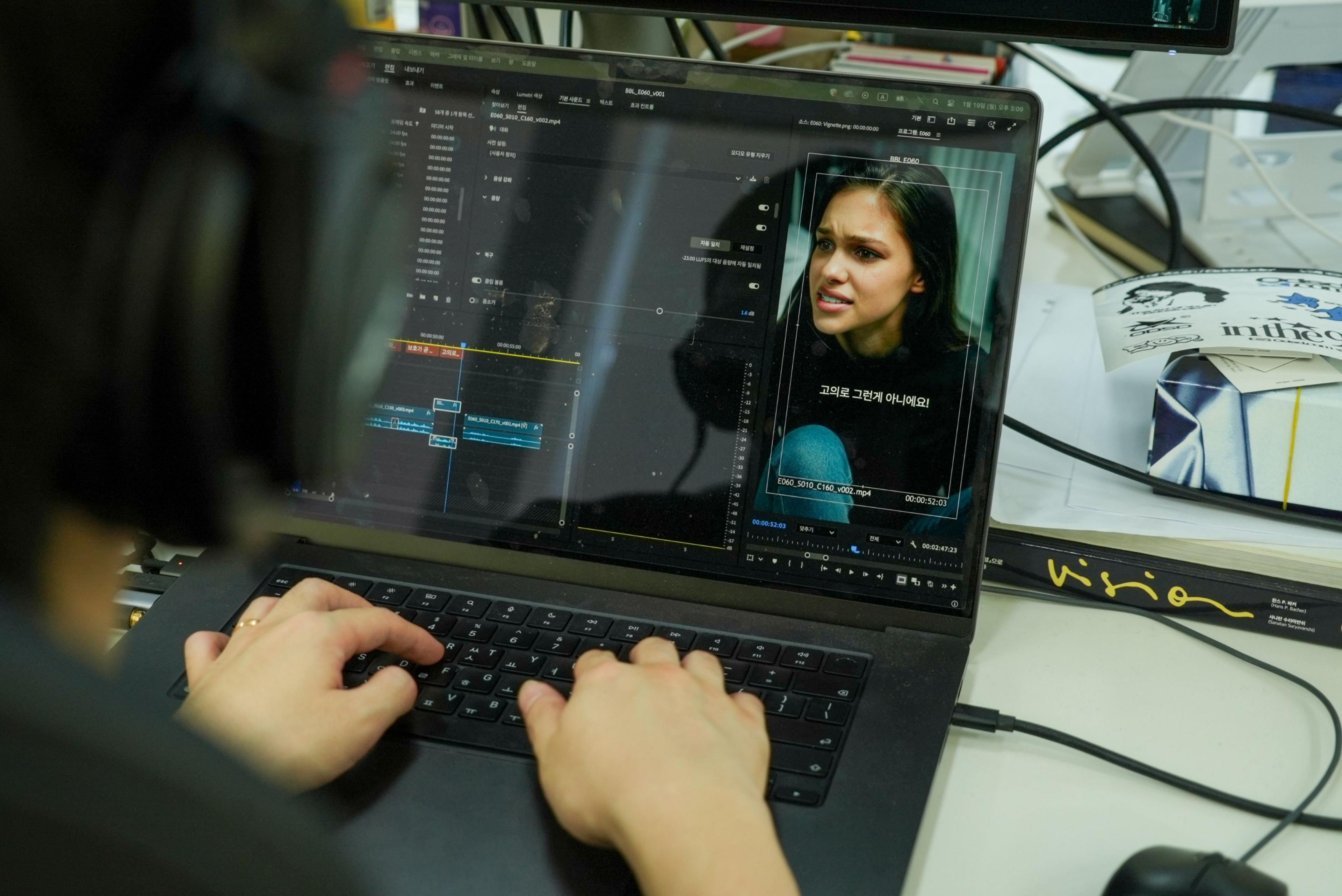 A woman's face is seen on a laptop screen in editing software, with the computer user's head and hands visible.