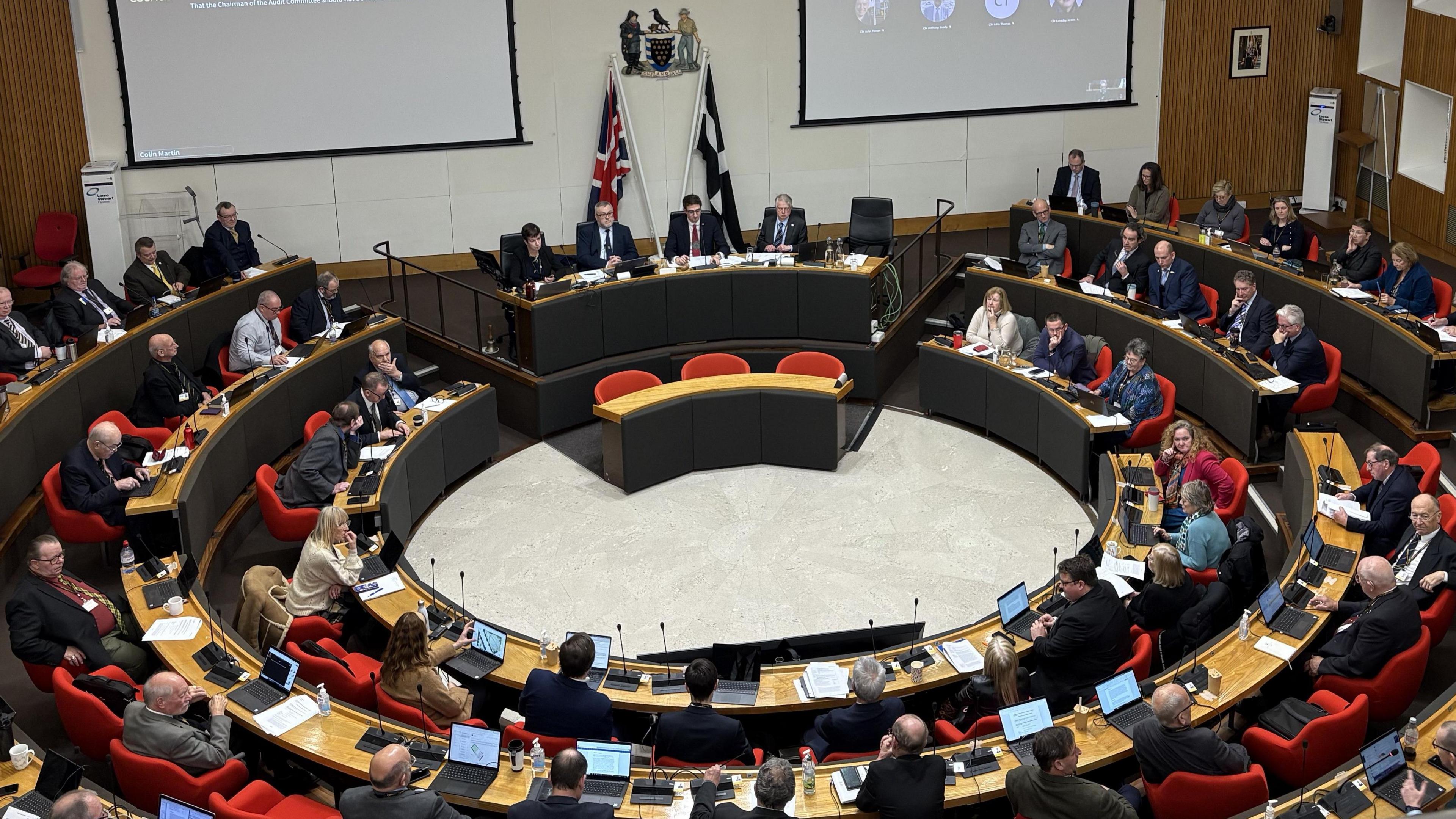 Councillors sitting on seats in circular chamber with the flags of Cornwall and the UK behind them