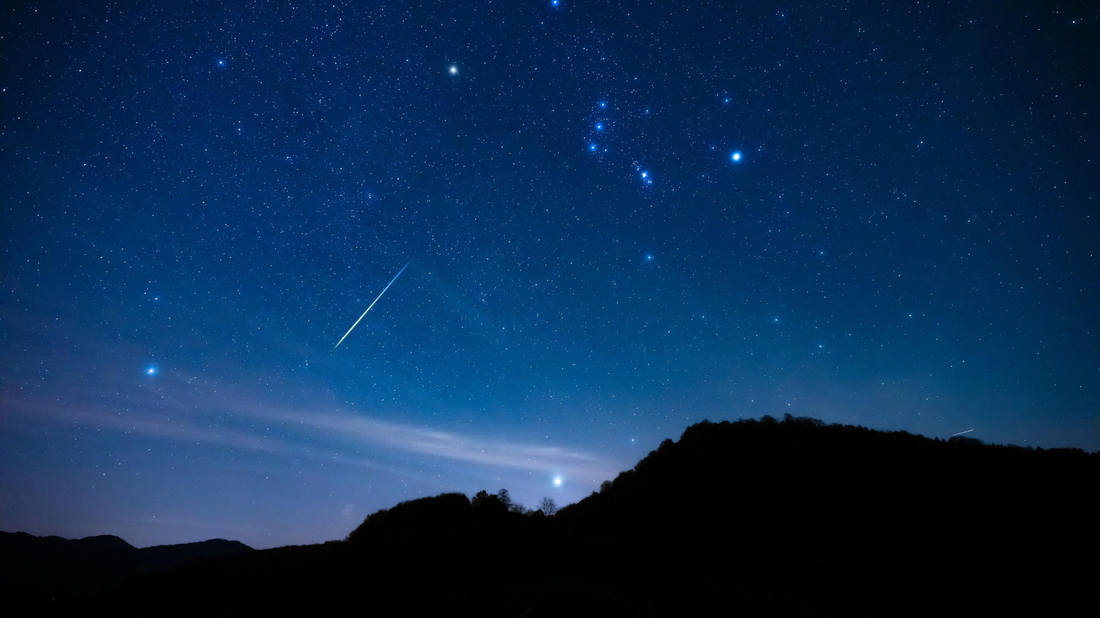 Blue night sky with Milky Way stars with Orionids meteor shower trails and countryside tree silhouettes