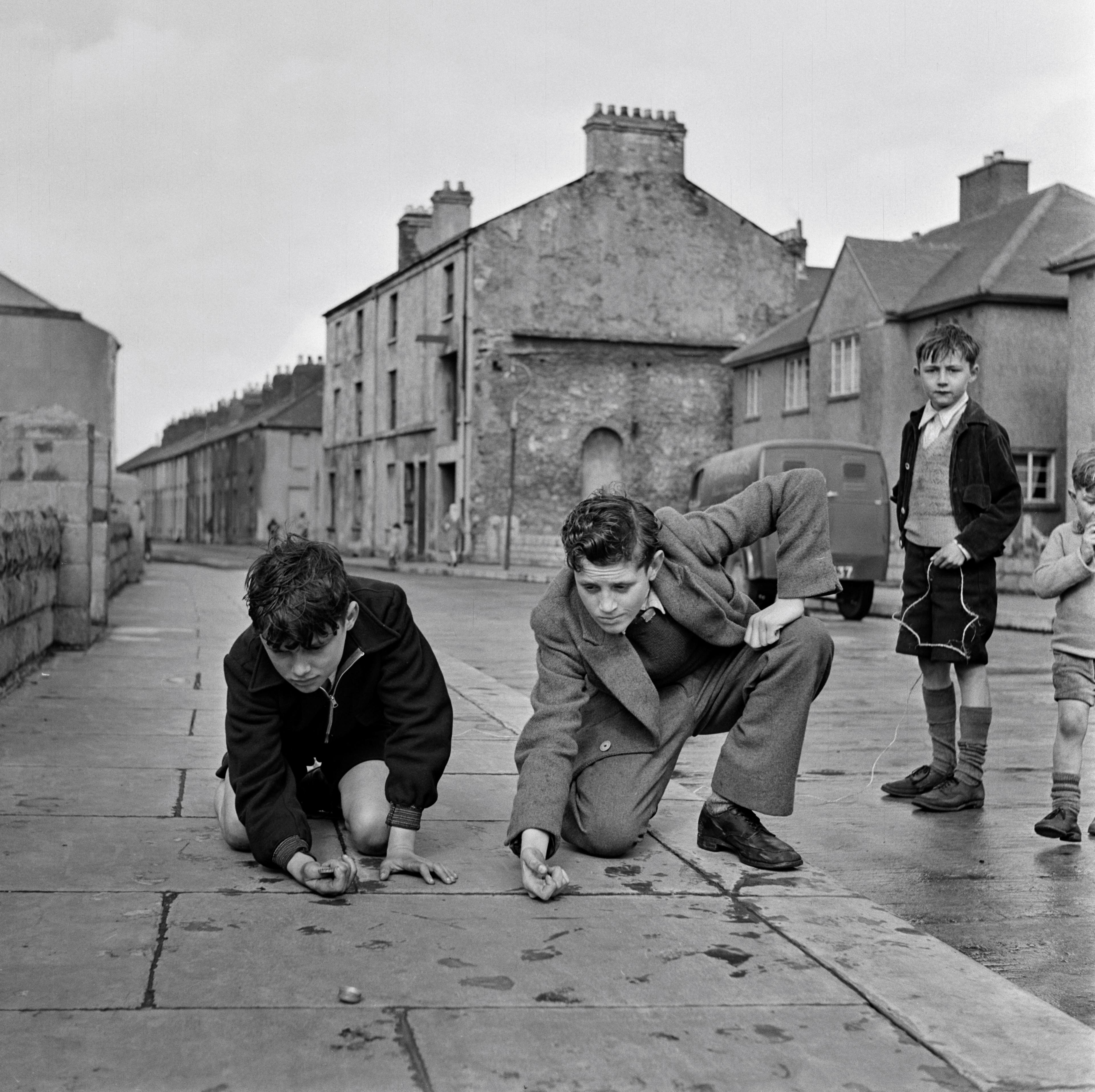 Boys dressed in blazers playing with marbles on a residential street