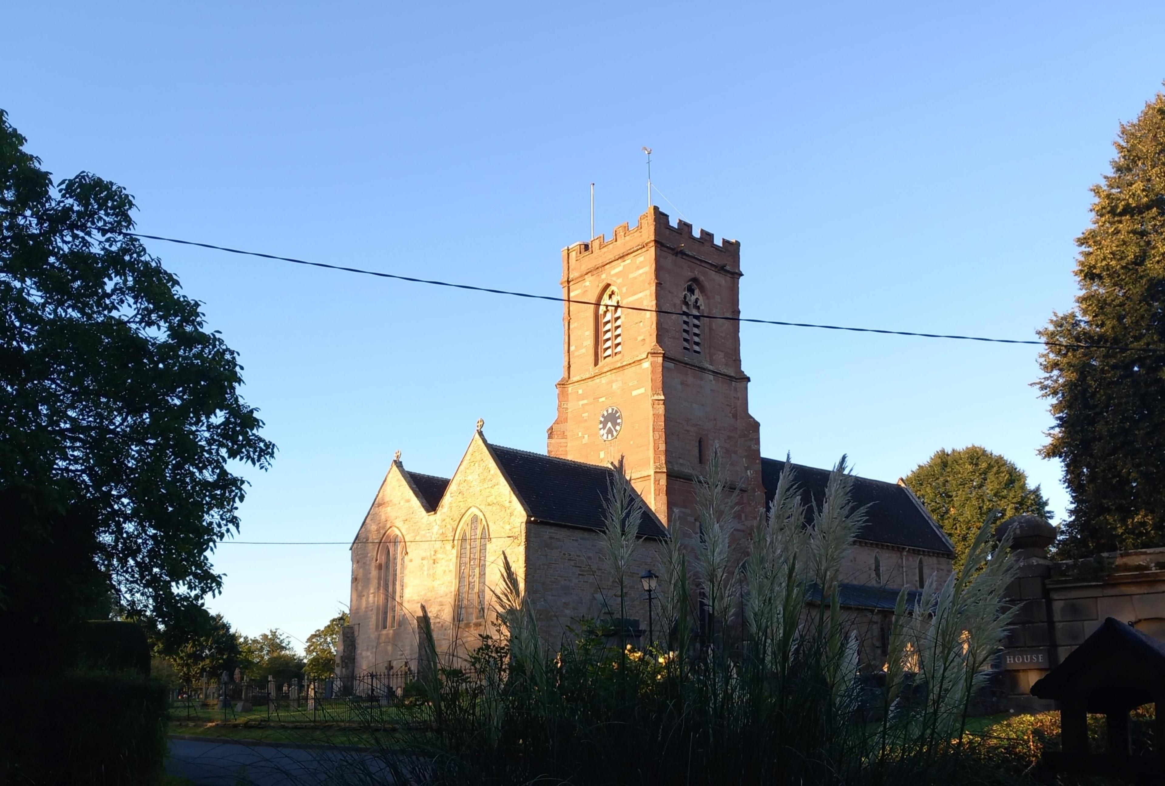 A stone-built church tower with sunlight on one face and deep shade in other directions. The sky behind is clear blue.