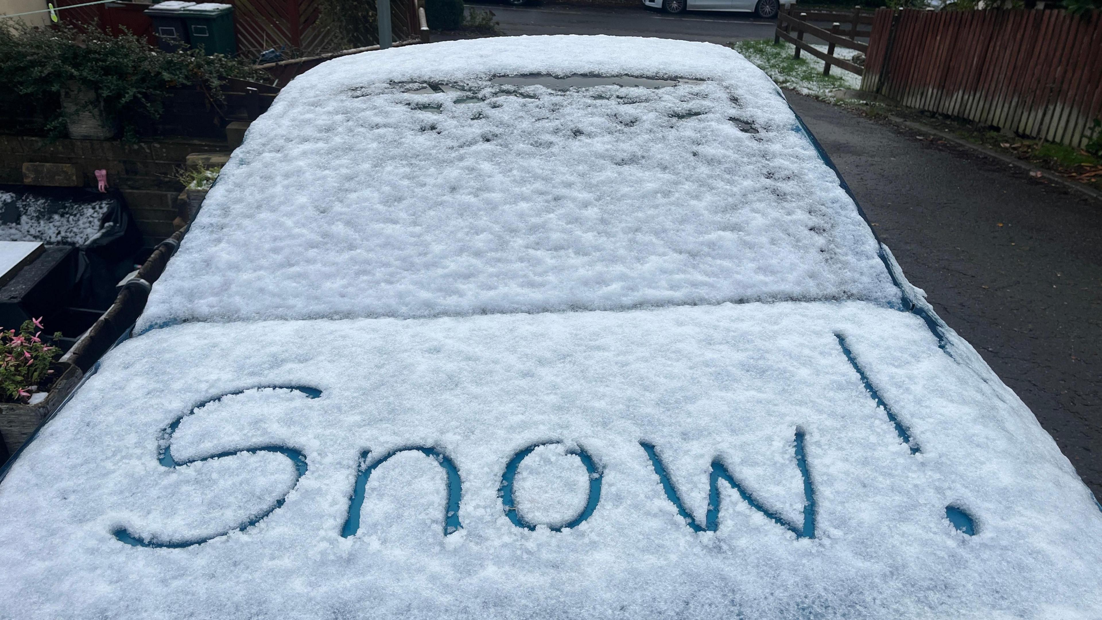 The words snow are etched out into a snow covered back of a car