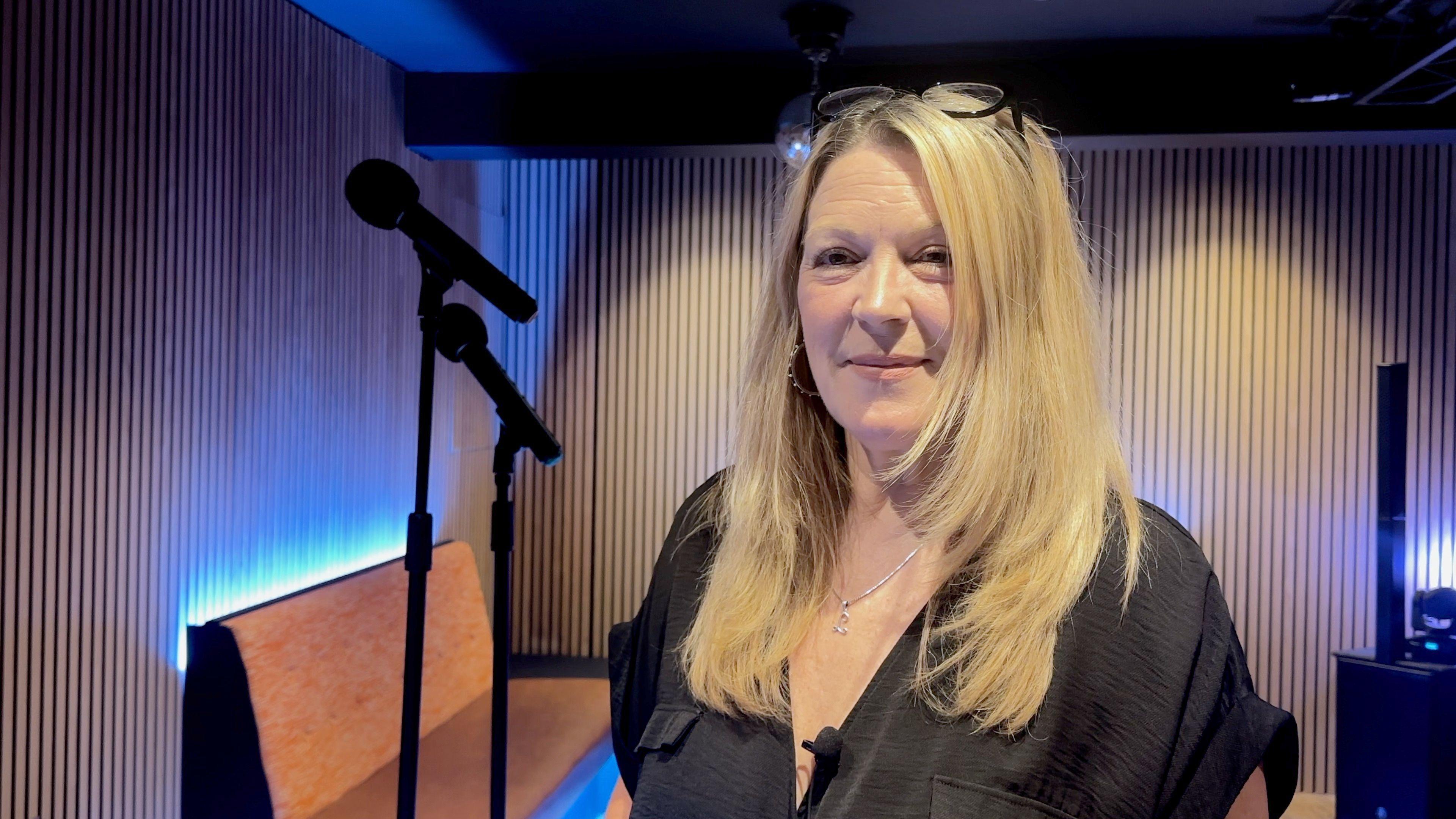 Lisa Duval, wearing a black shirt, standing next to two wireless microphones in a karaoke room.