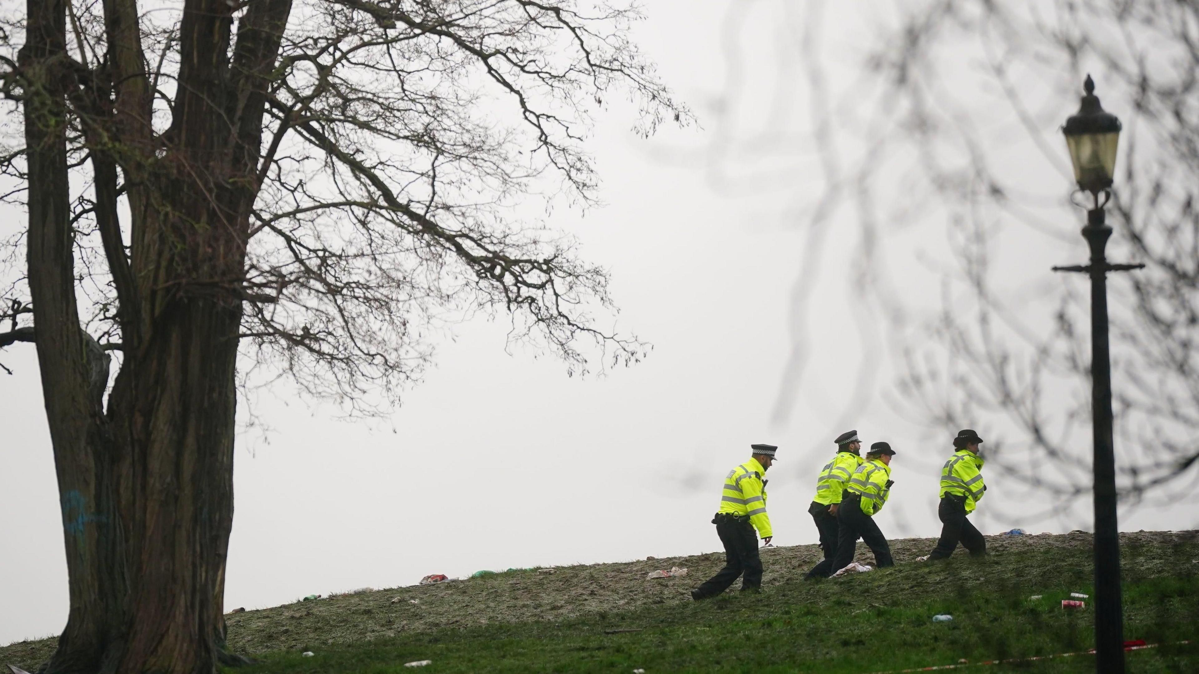 Image from January 2024 showing four uniformed police officers walking across Primrose Hill after the fatal attack, with a lamp post and tree visible in the foreground