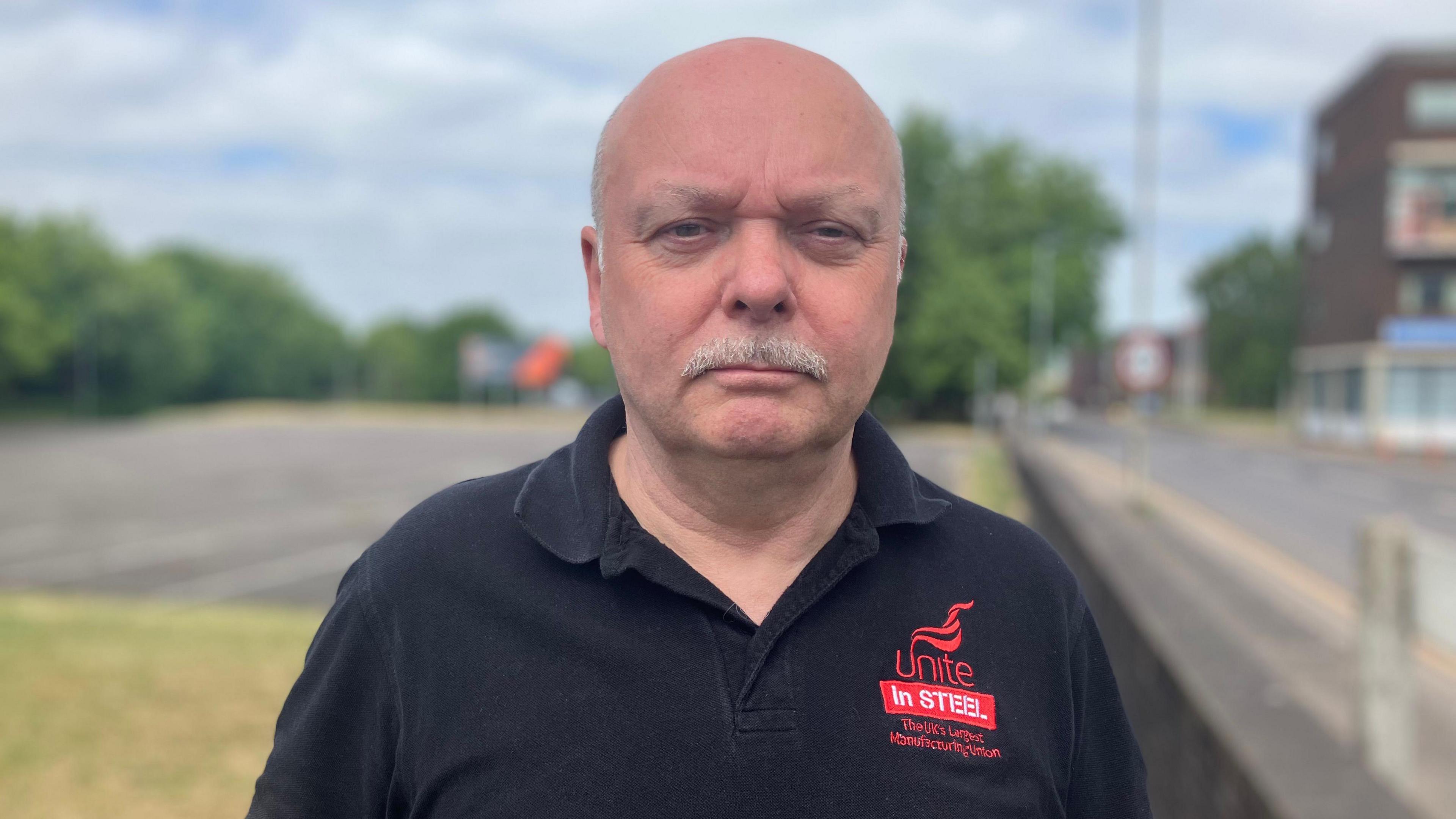 Mr Foster wears a black top with "Unite in Steel" red logo on it.