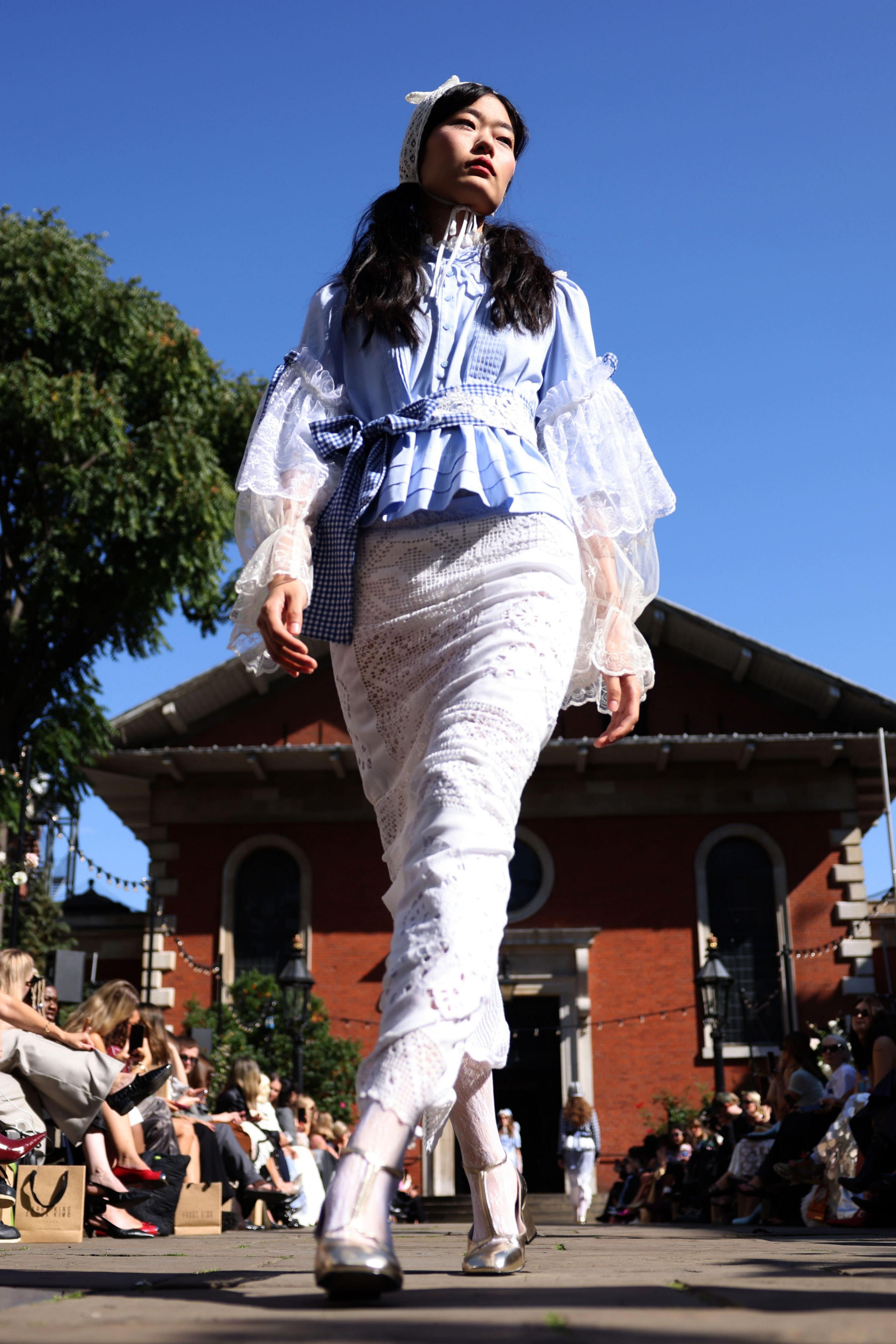 A model walks the catwalk outside St. Pauls Church in Covent Garden, dress in a white skirt, silver heels and a blue top.