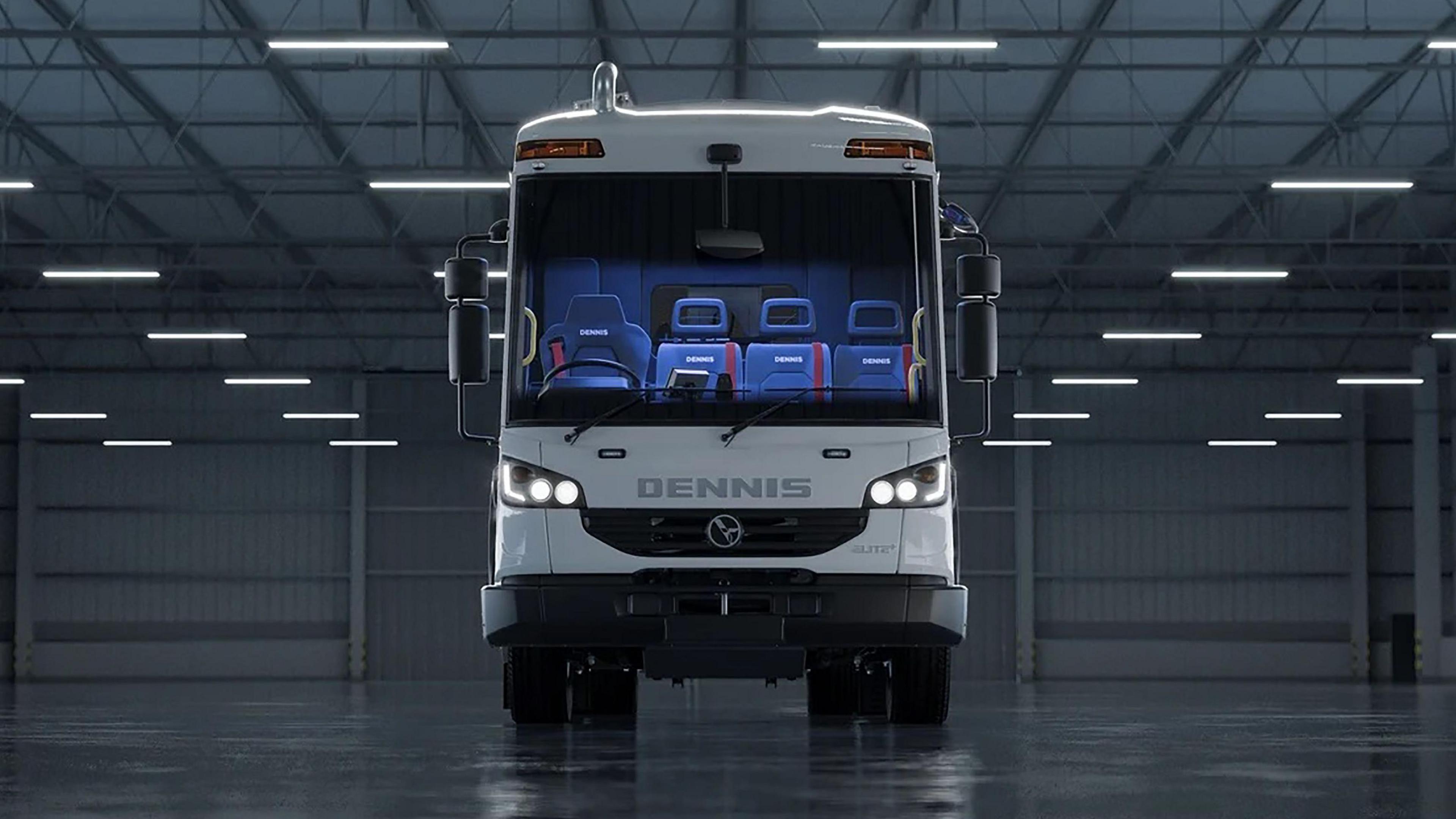 Picture is taken of a Dennis Eagle lorry looking straight on - it is white and has the letters DENNIS across the front in capitals. Its lights are on and there are four seats in the truck, all are blue with red seatbelts