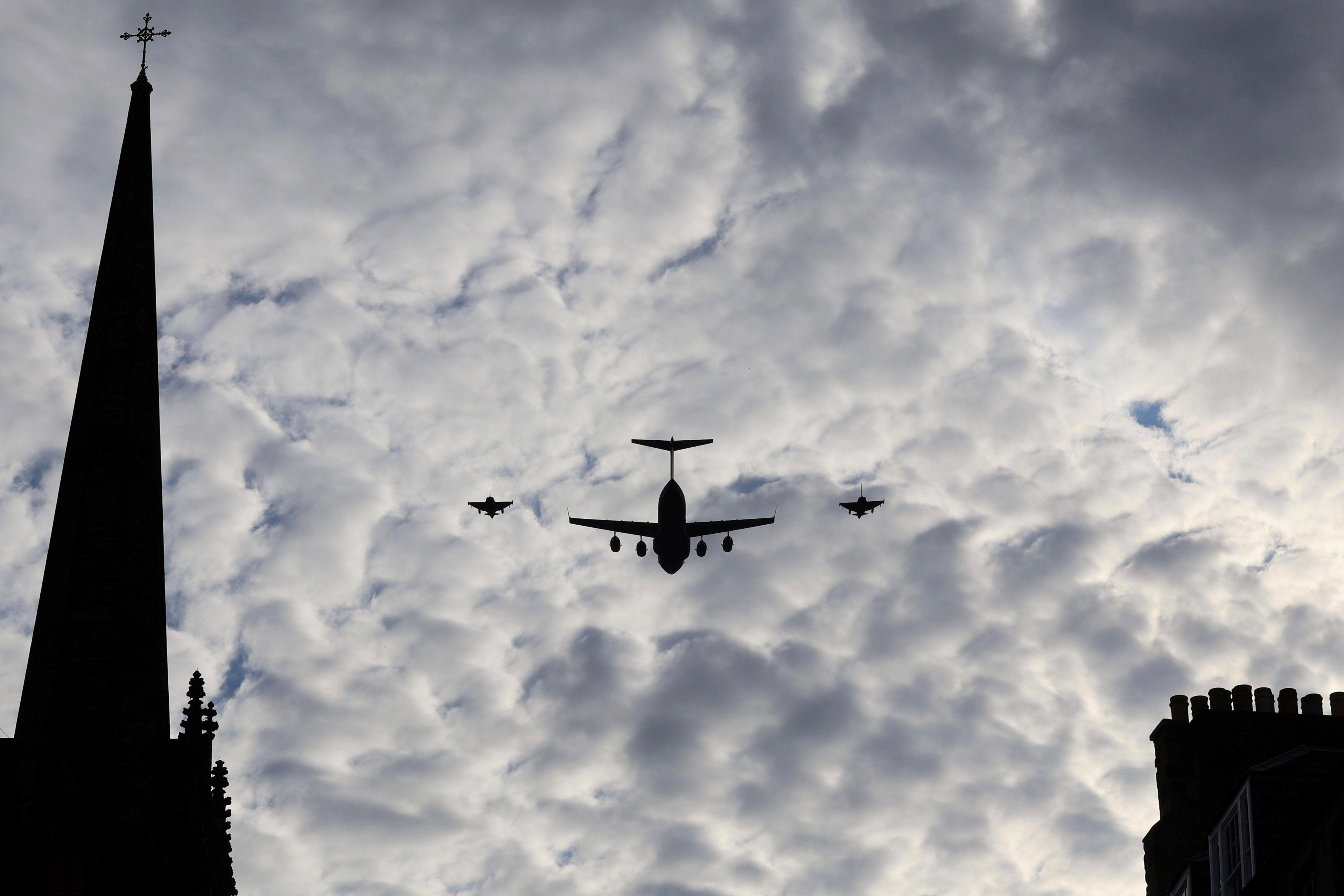 Three military aircraft silhouetted in a cloudy sky, alongside a steeple and chimneys.