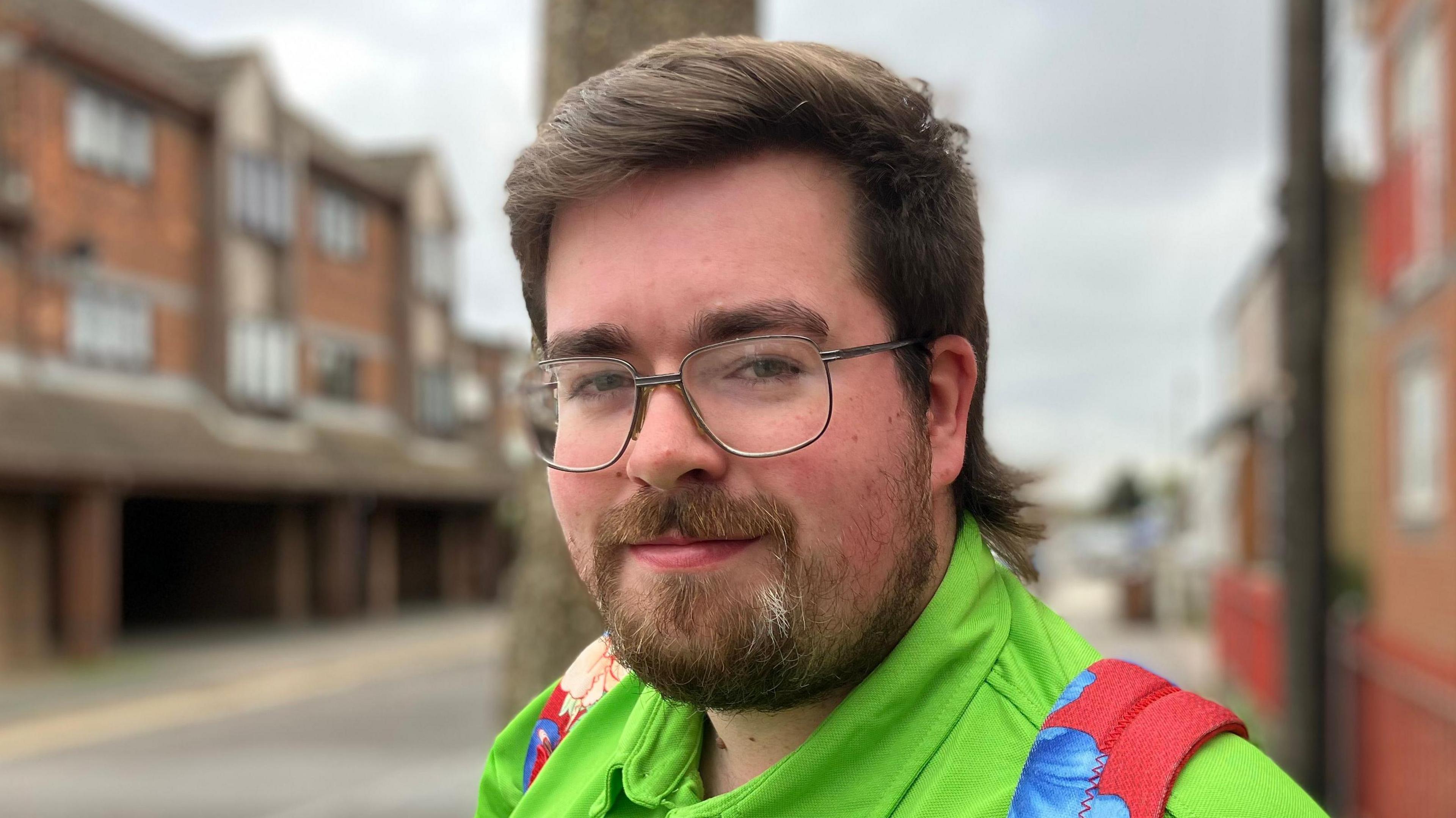 A man wearing glasses and a bright green jacket. He is smiling at the camera