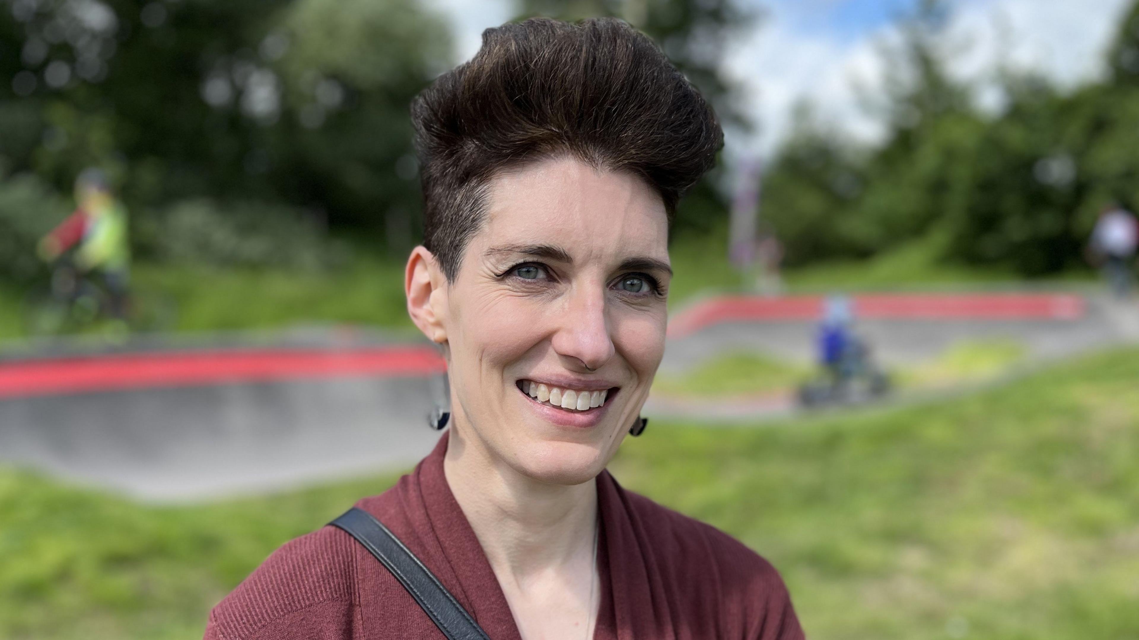 Alexandra Knox with short black hair, smiling, with the pump track behind her