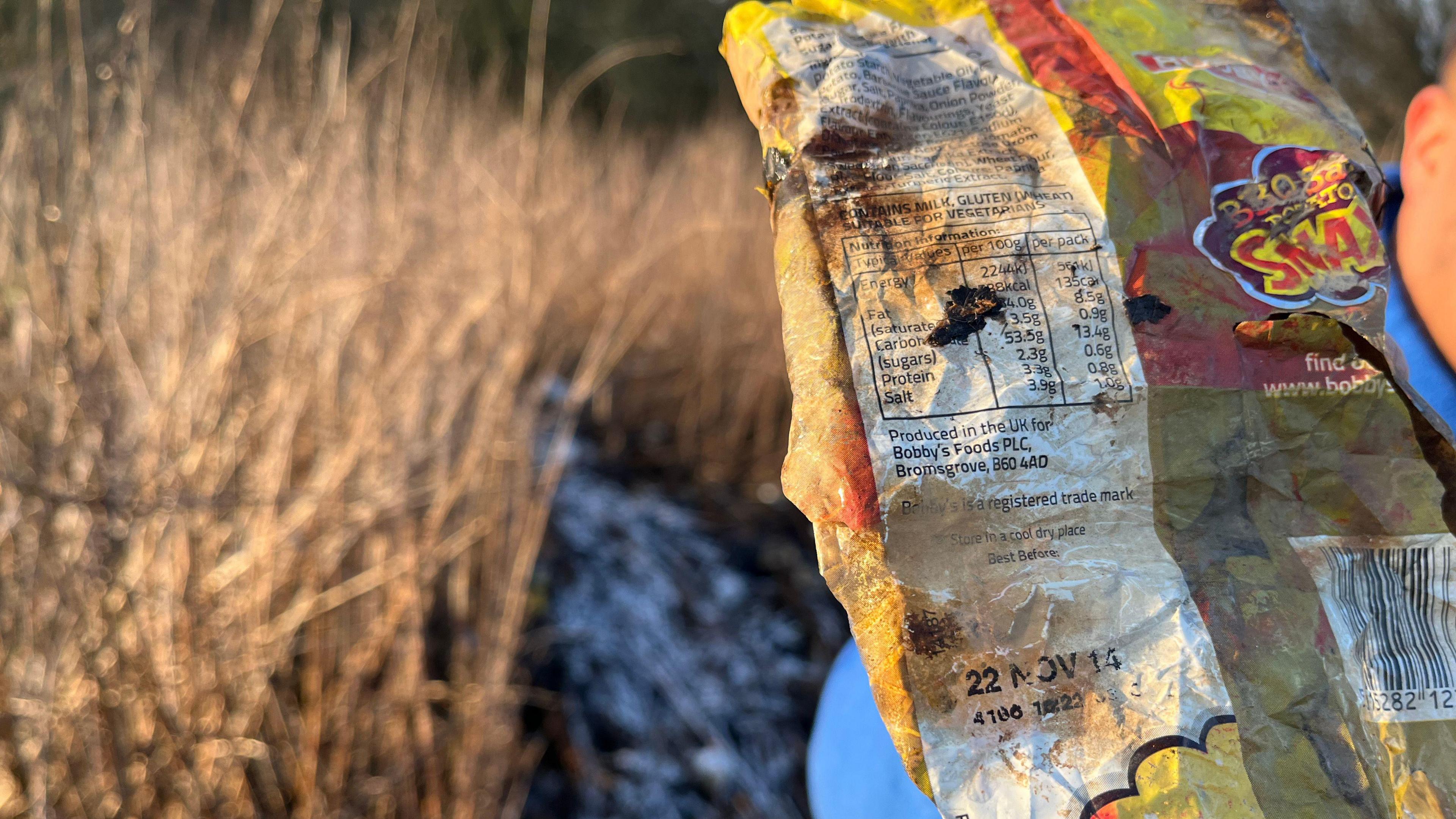 A muddy, old packet of BBQ SNAX crisps, with a sell-by date of 2014