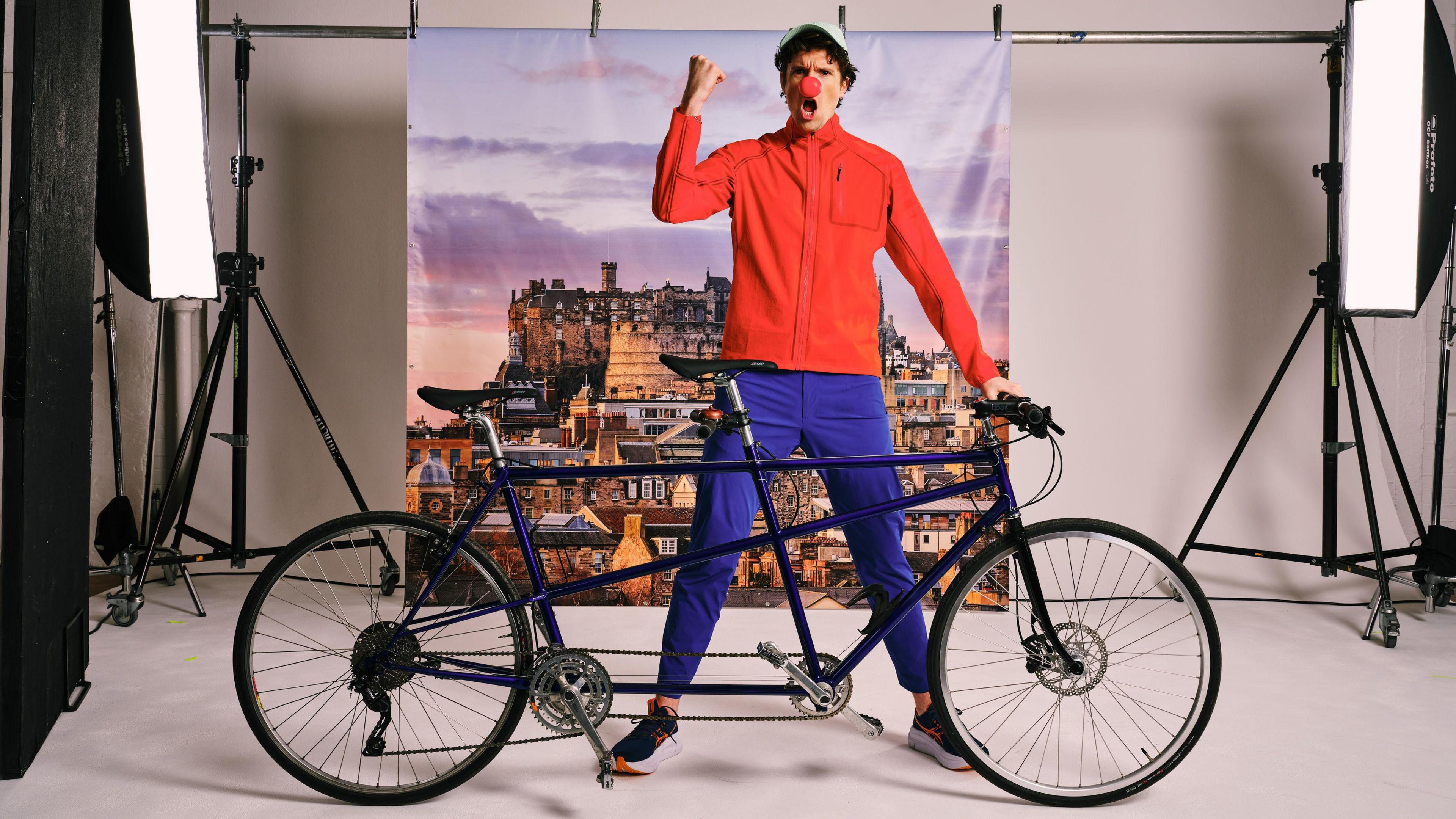 greg james wearing a red nose and standing next to a bike.